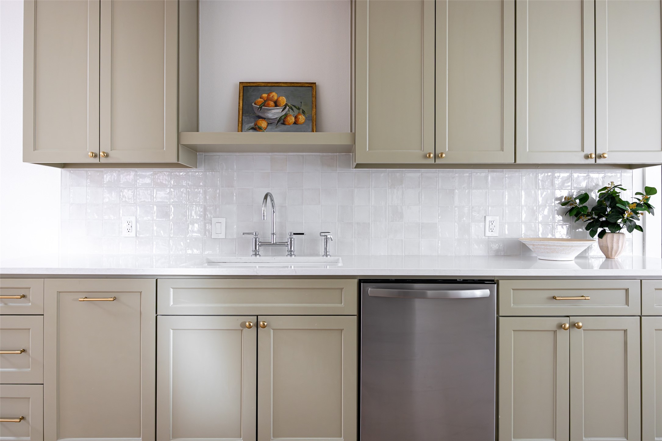 Kitchen with taupe shaker cabinets, glossy white tile backsplash, and stainless steel dishwasher.