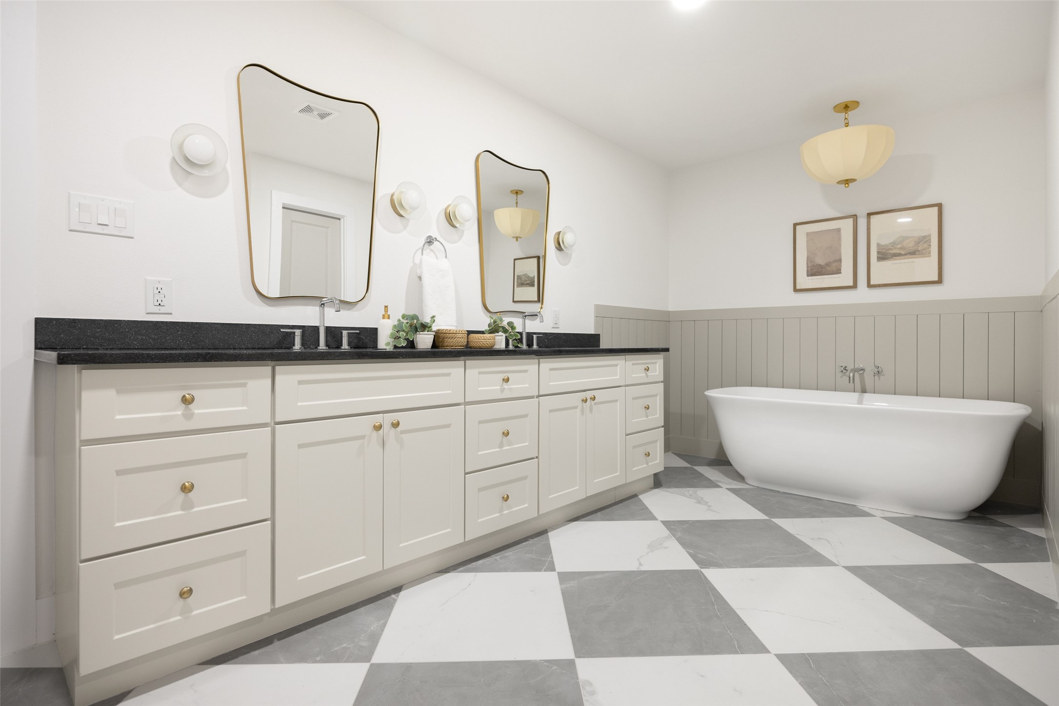 Bathroom with a long white vanity, brass-framed mirrors, freestanding tub, and checkerboard tile floor.