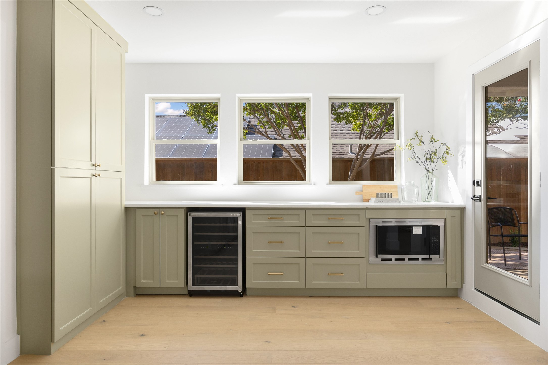 Kitchen with sage-green built-ins, a wine refrigerator, and windows overlooking a fenced yard.