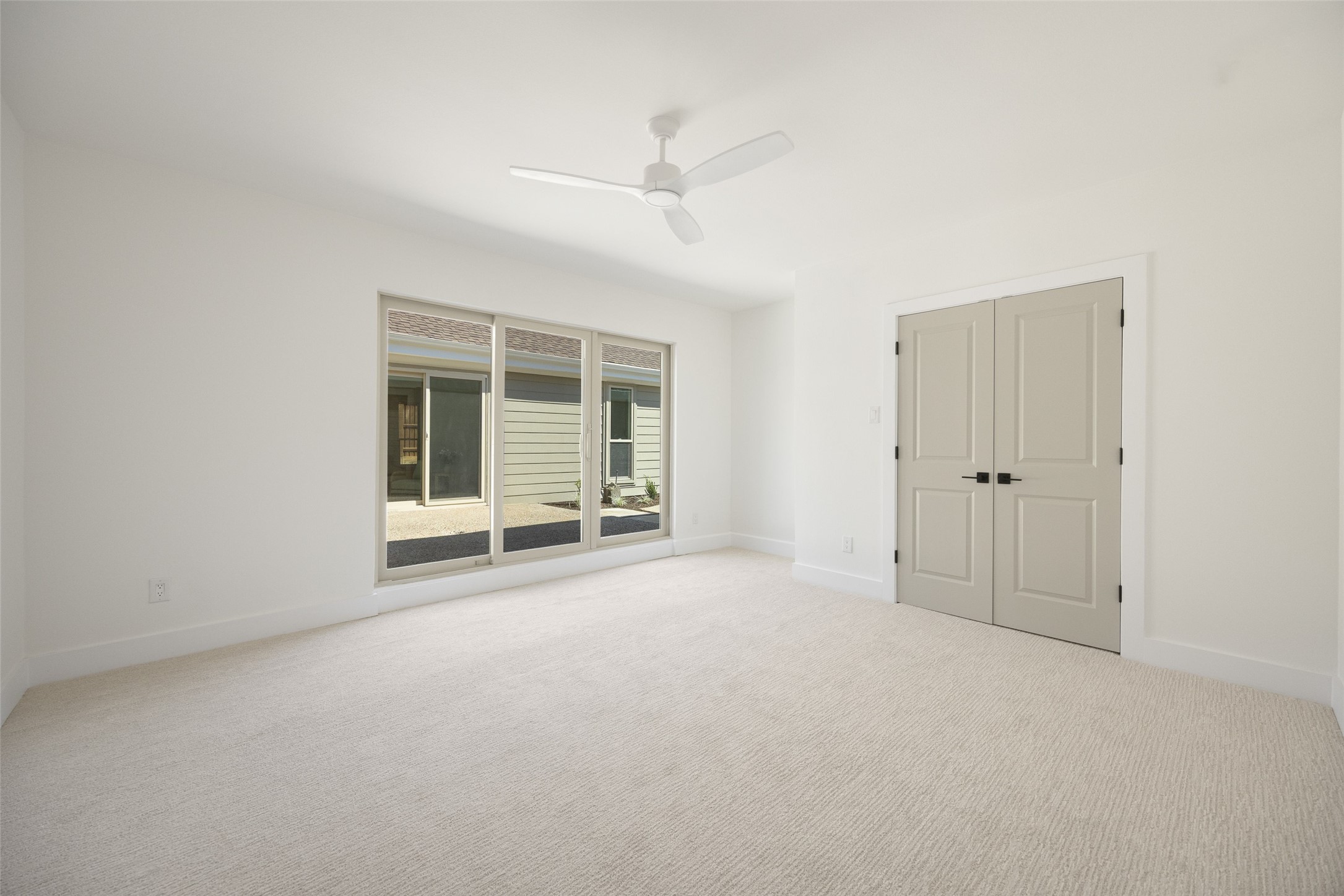 Empty carpeted bedroom with sliding glass doors, double closet doors, and a ceiling fan