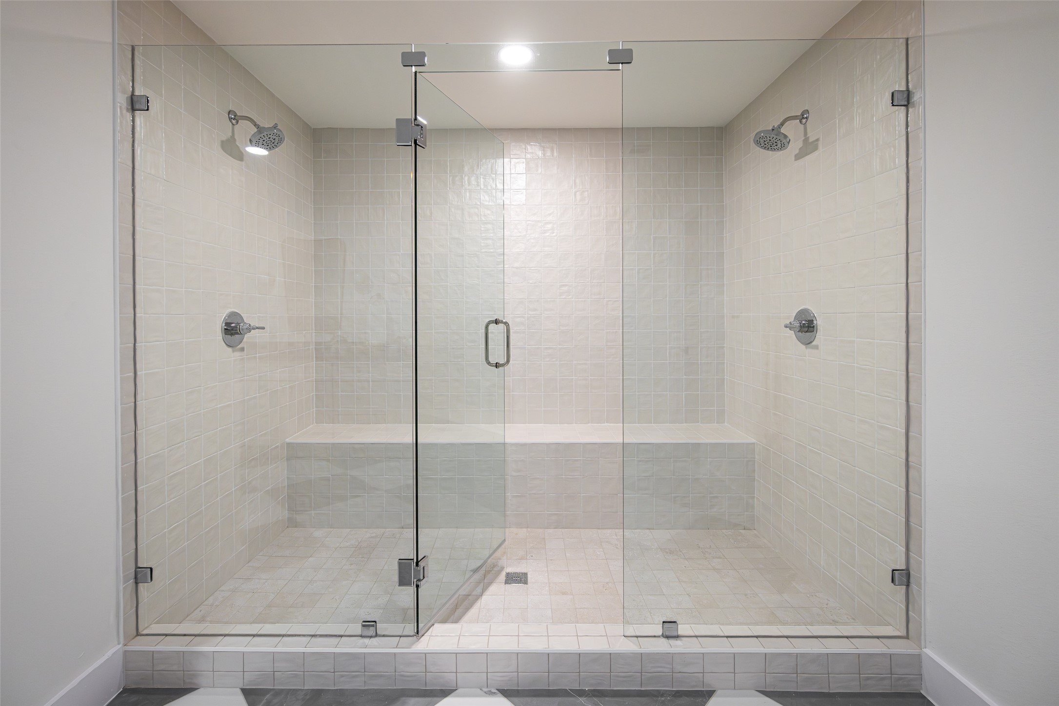 Walk-in shower with a glass enclosure, two showerheads, and a built-in tiled bench.