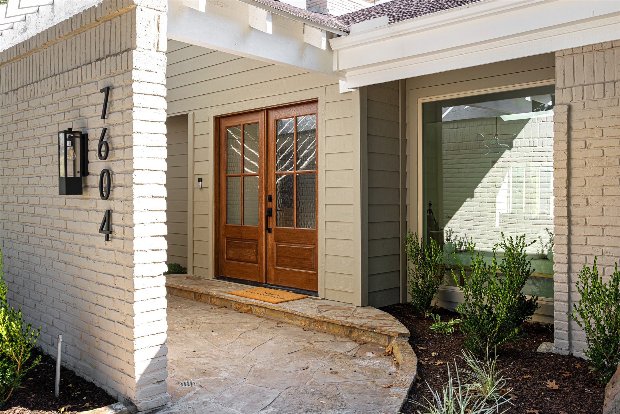 Front entrance with wood-and-glass double doors, white brick, and a curved stone-paved porch.