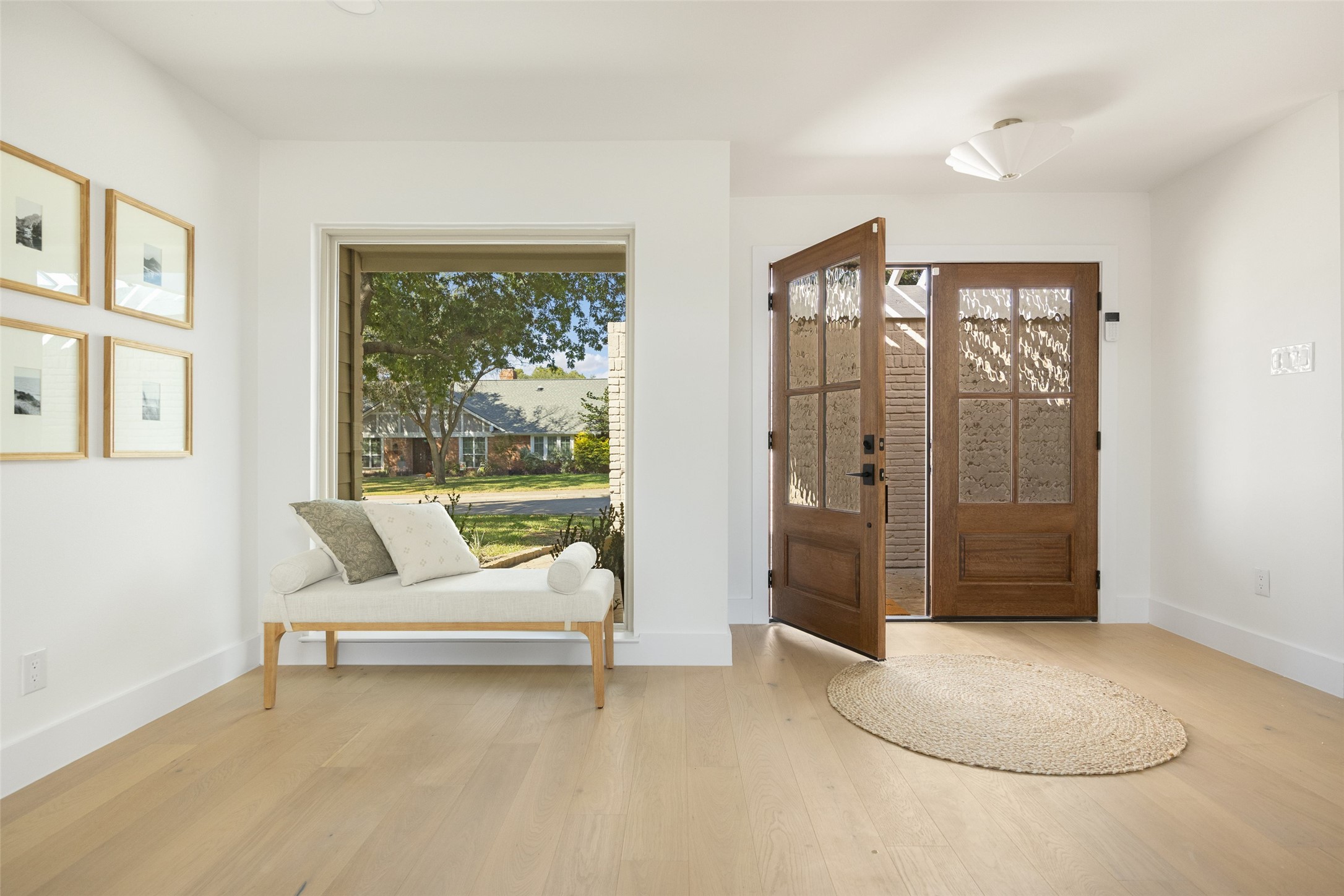 Bright entryway with a white bench, light wood floors, and open wooden front doors.