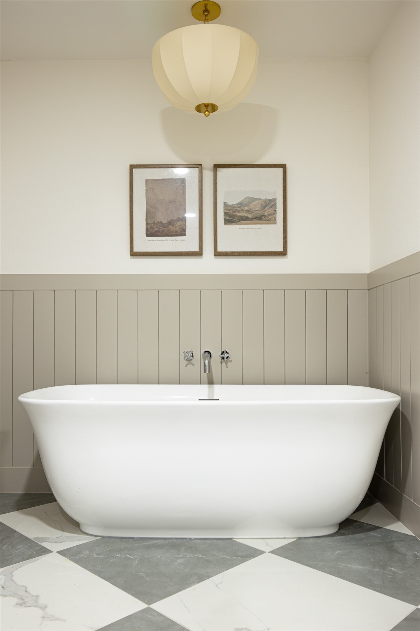 Bathroom with a freestanding white tub, paneled walls, framed art, and checkerboard marble flooring.