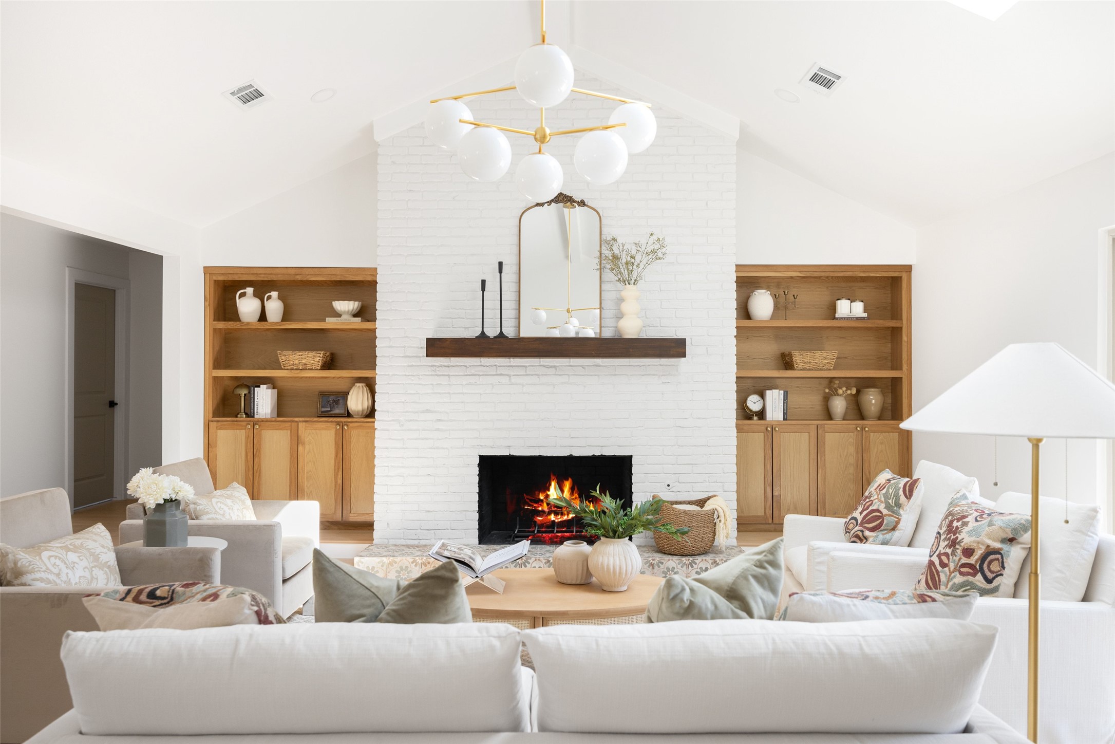 Staged living room with a white brick fireplace, oak built-ins, and a vaulted ceiling.