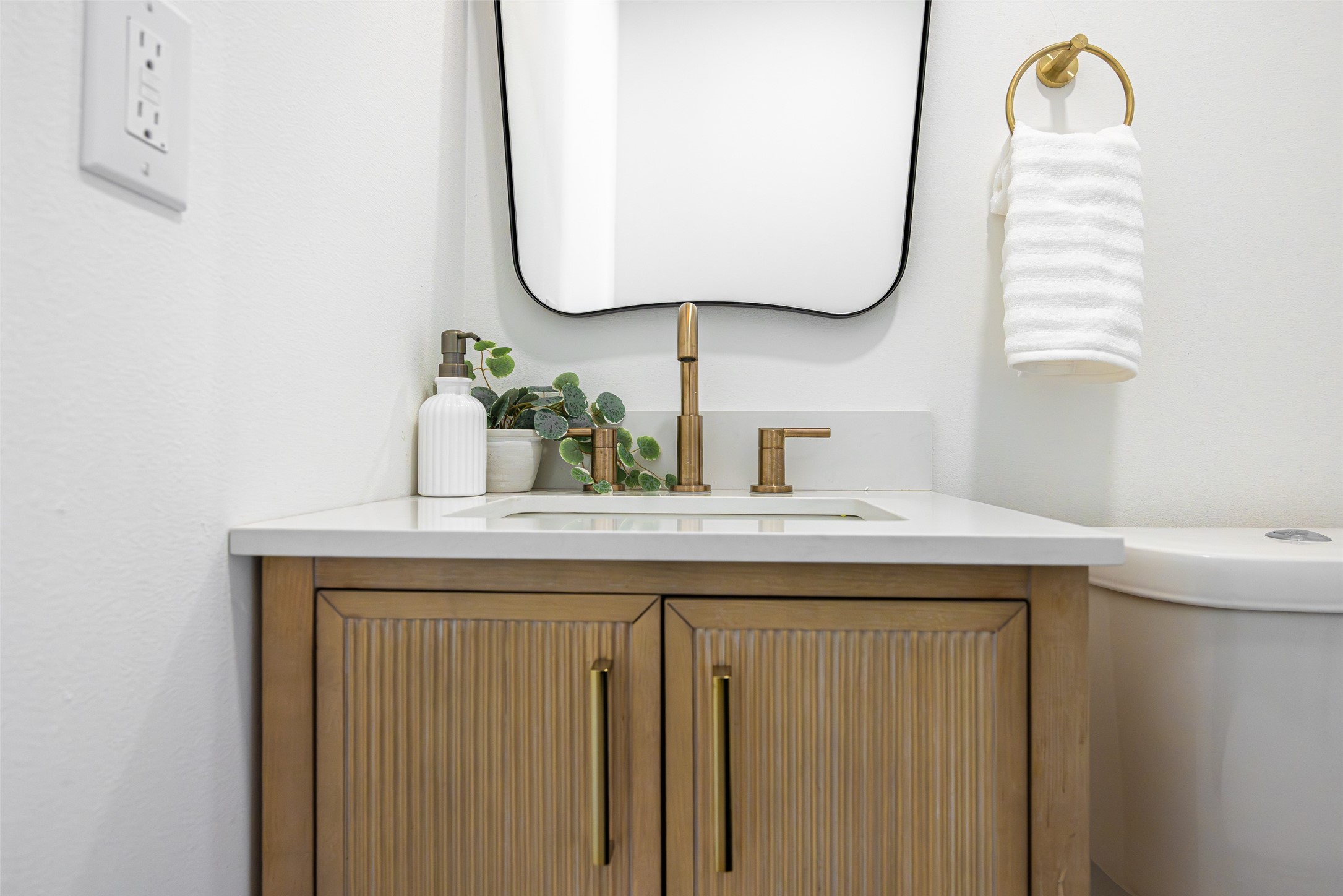 Bathroom vanity with brass fixtures, fluted wood cabinet doors, and a white towel beside the sink.