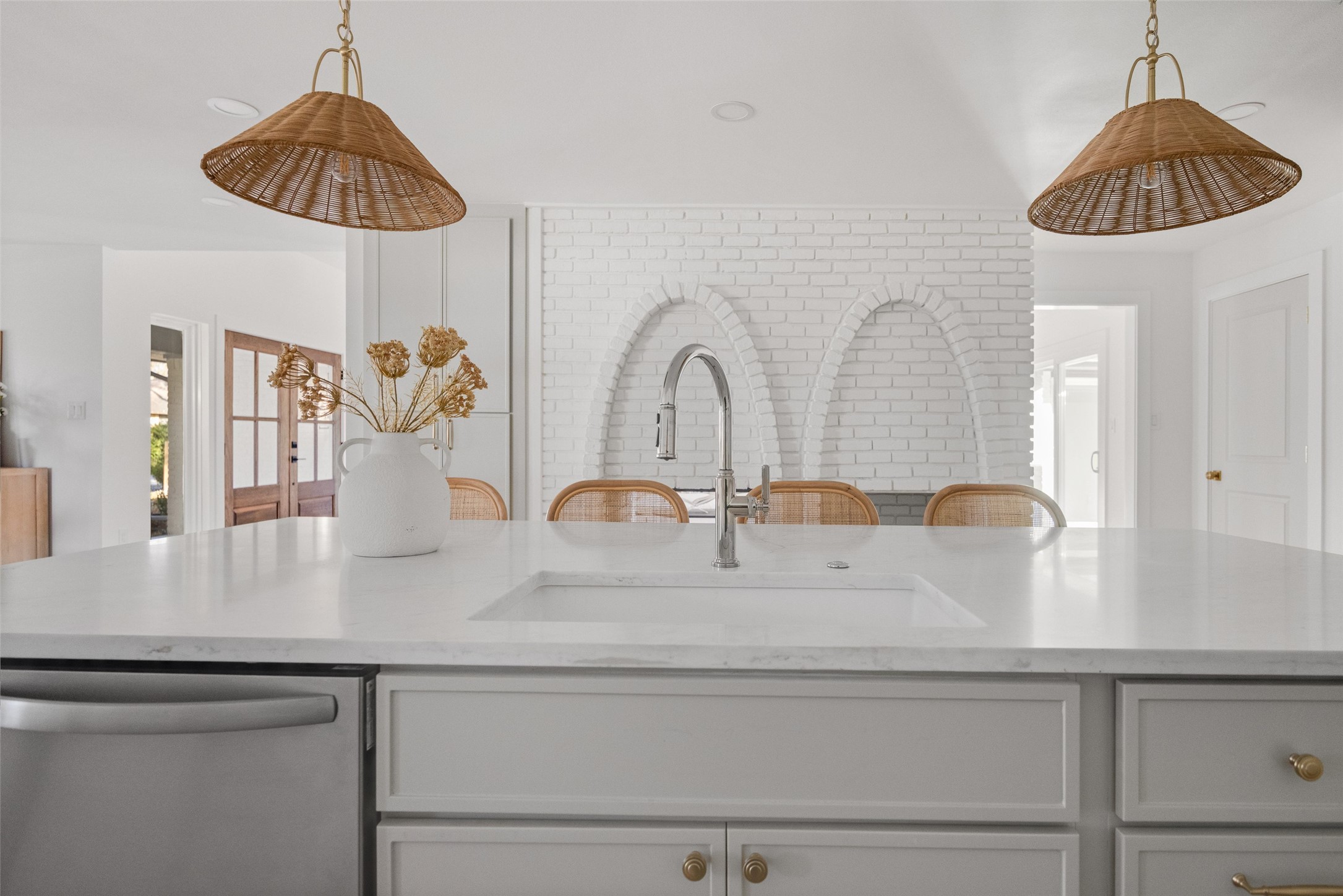 Bright white kitchen with a large island, arched brick backsplash niches, and woven pendant lights.