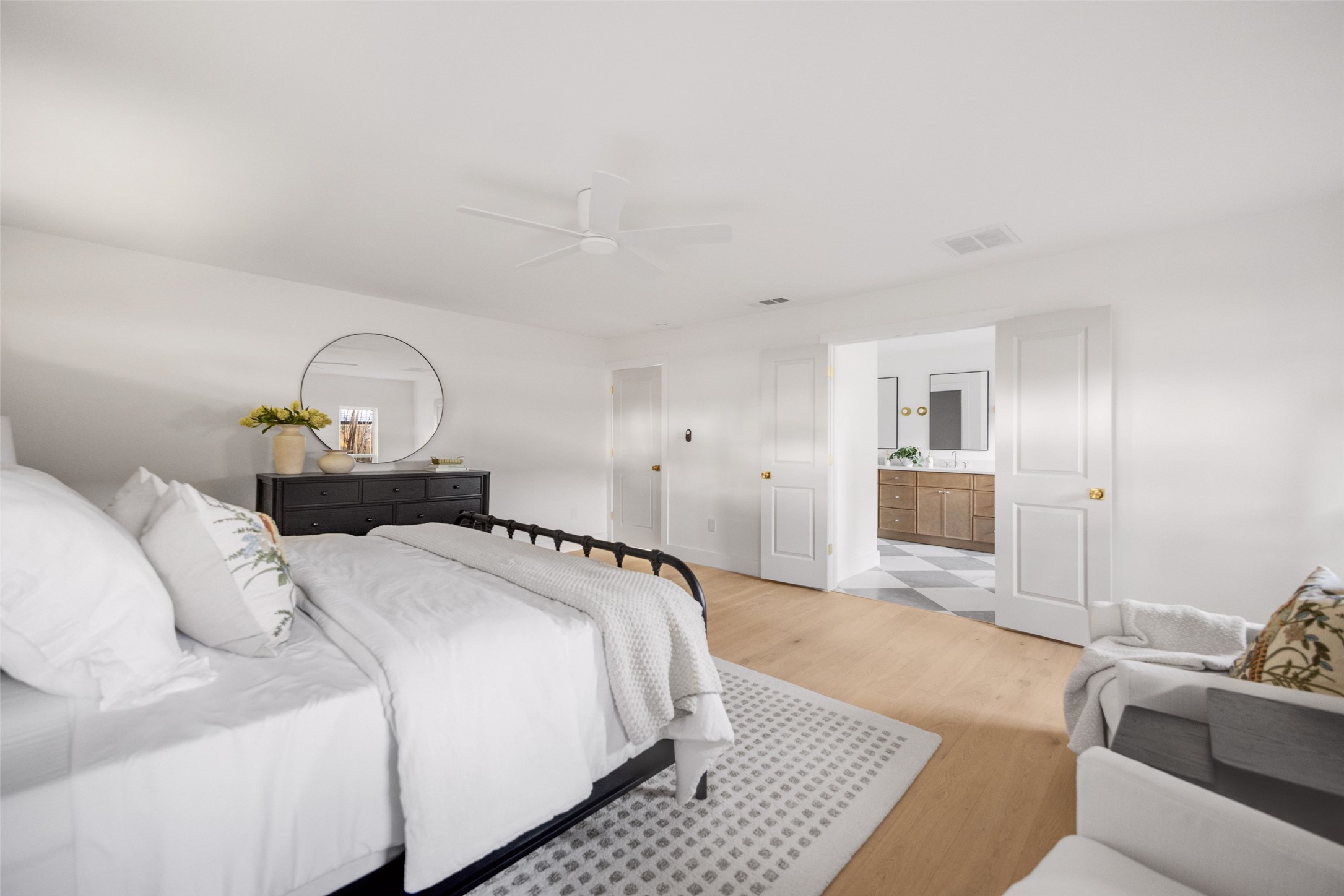 Bright bedroom with white bedding, a black metal bed, and open doors to an ensuite bathroom.