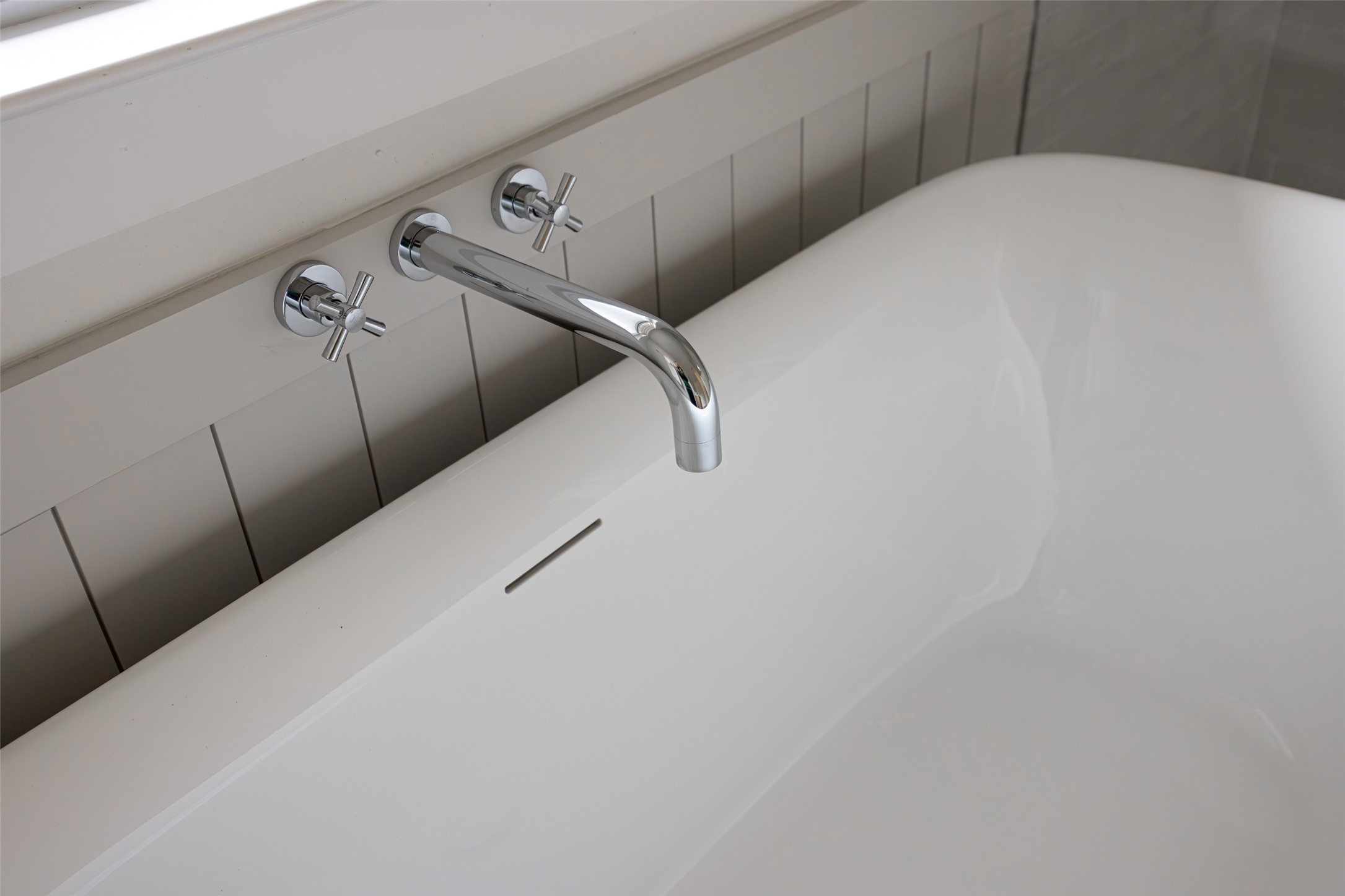 White bathtub with a polished chrome wall-mounted faucet and cross handles.