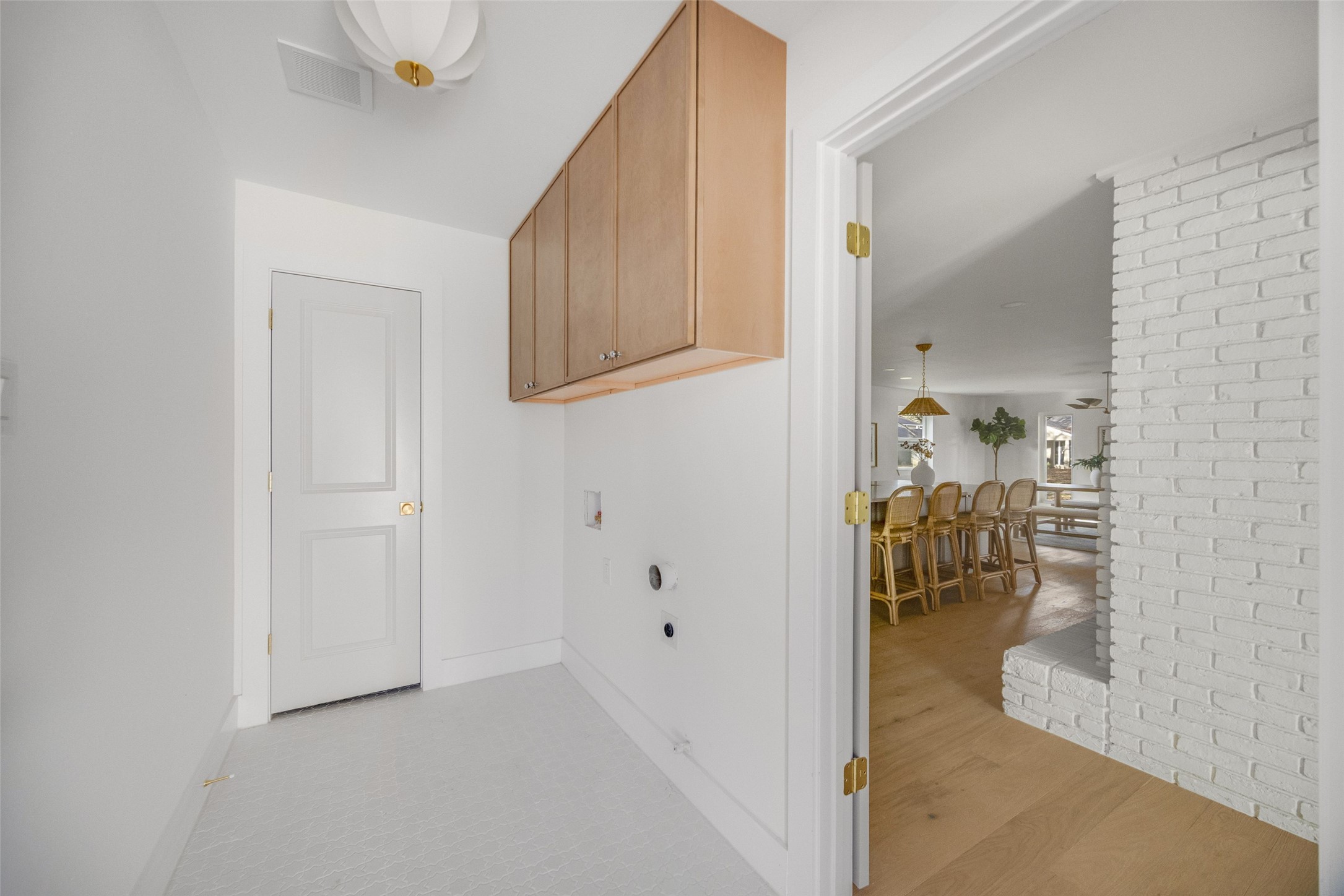Laundry room with wood cabinets and patterned tile flooring, opening to a dining area.