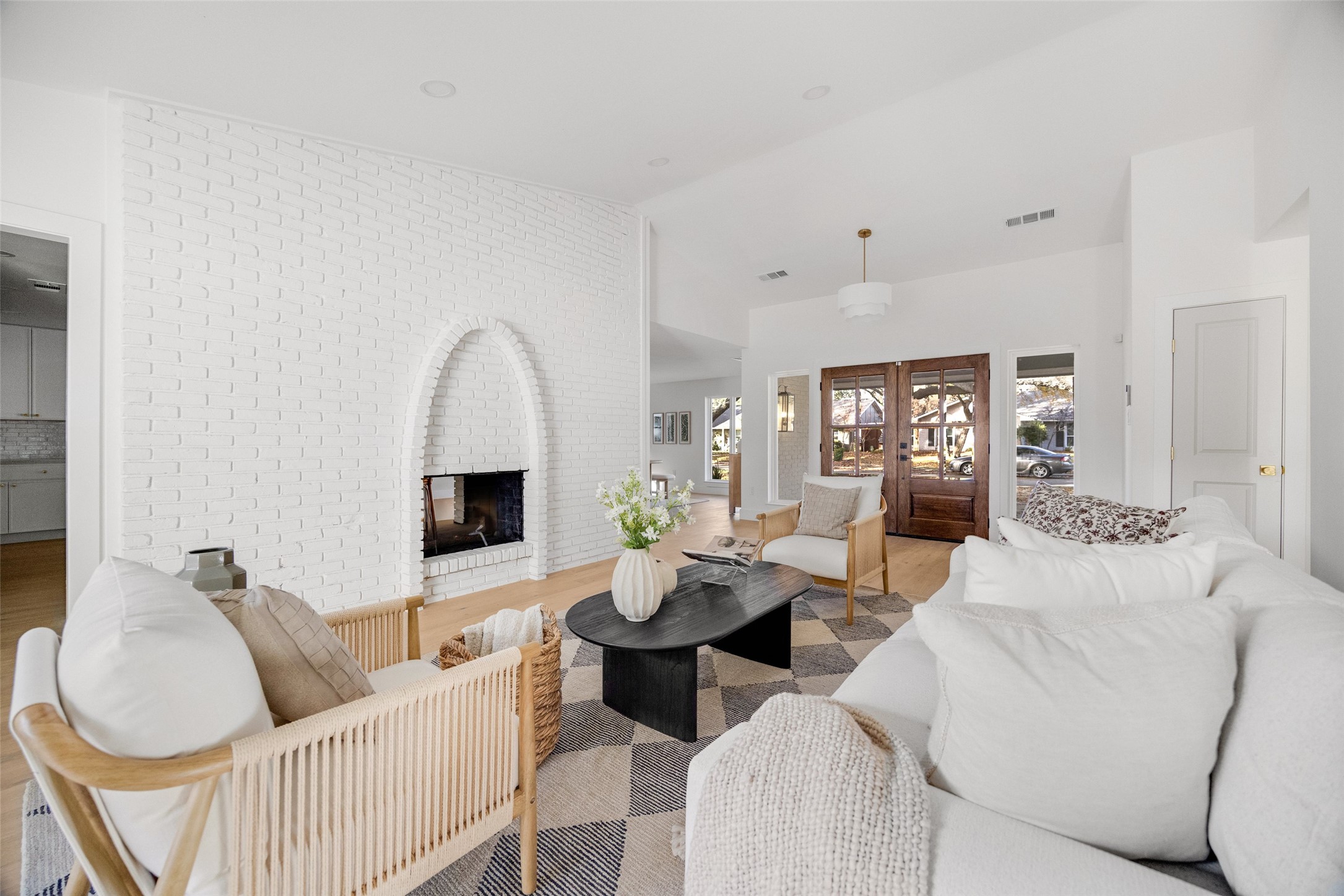 Living room with an arched white brick fireplace, white sofas, and wood-and-glass entry doors.