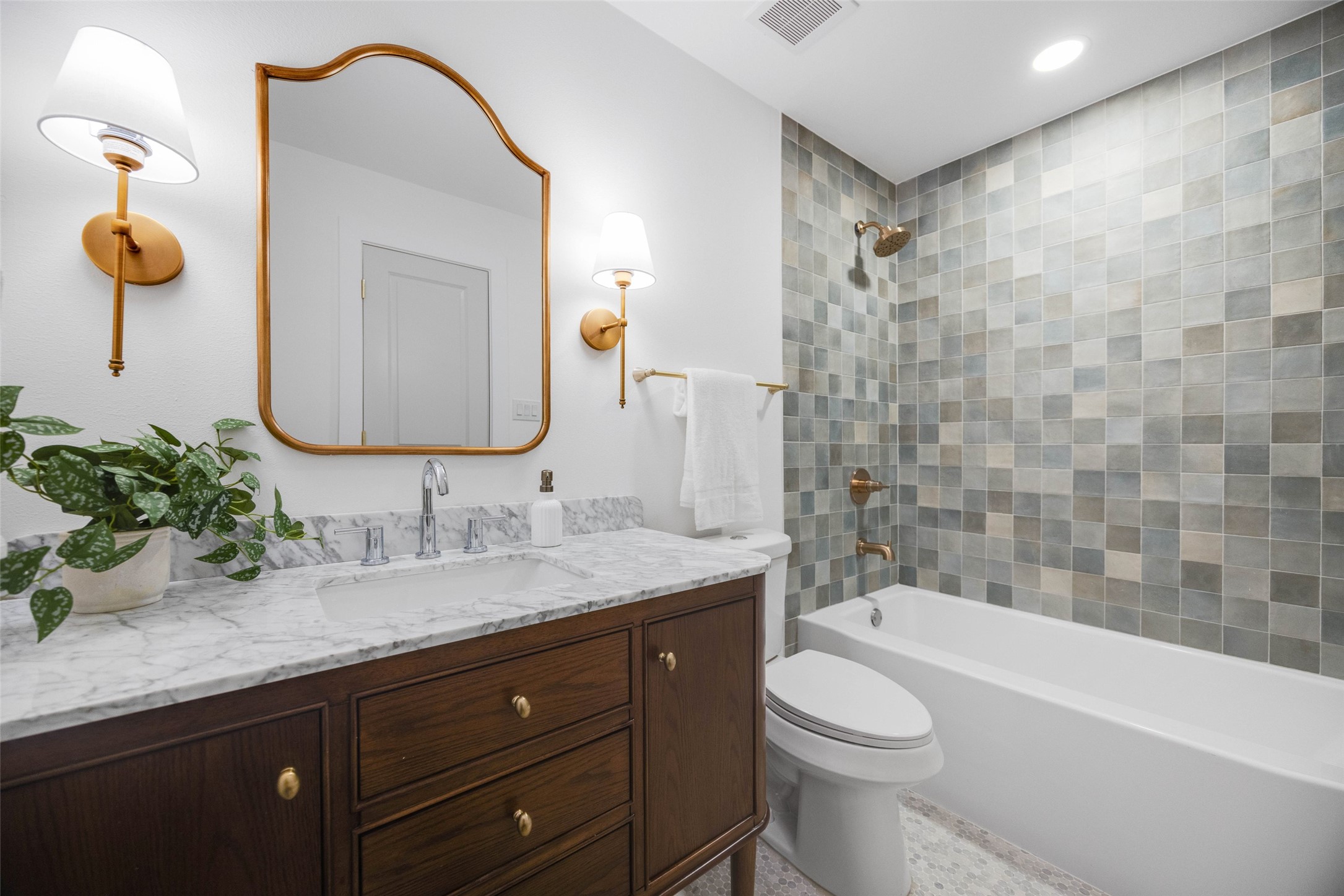 Bathroom with a marble-topped wood vanity and gray tiled tub surround.