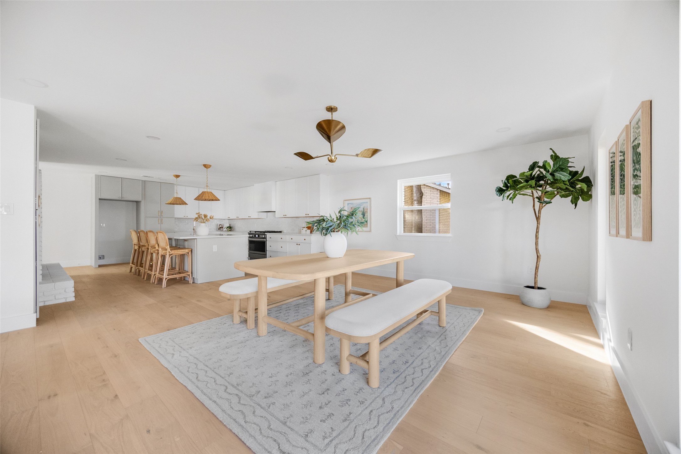 Open-plan kitchen and dining area with white cabinets, rattan stools, and a pale wood table with benches.