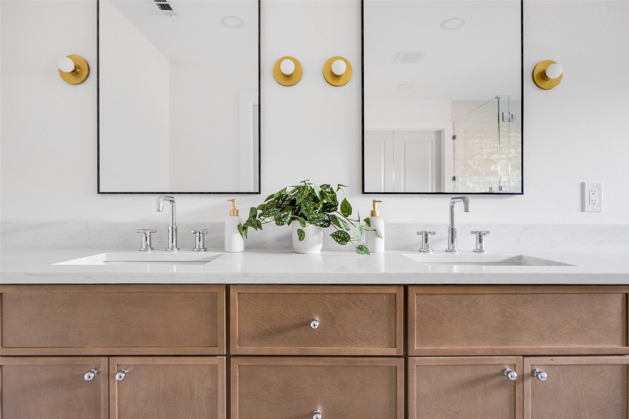 Bathroom vanity with double sinks, wood cabinets, large mirrors, and gold sconces.