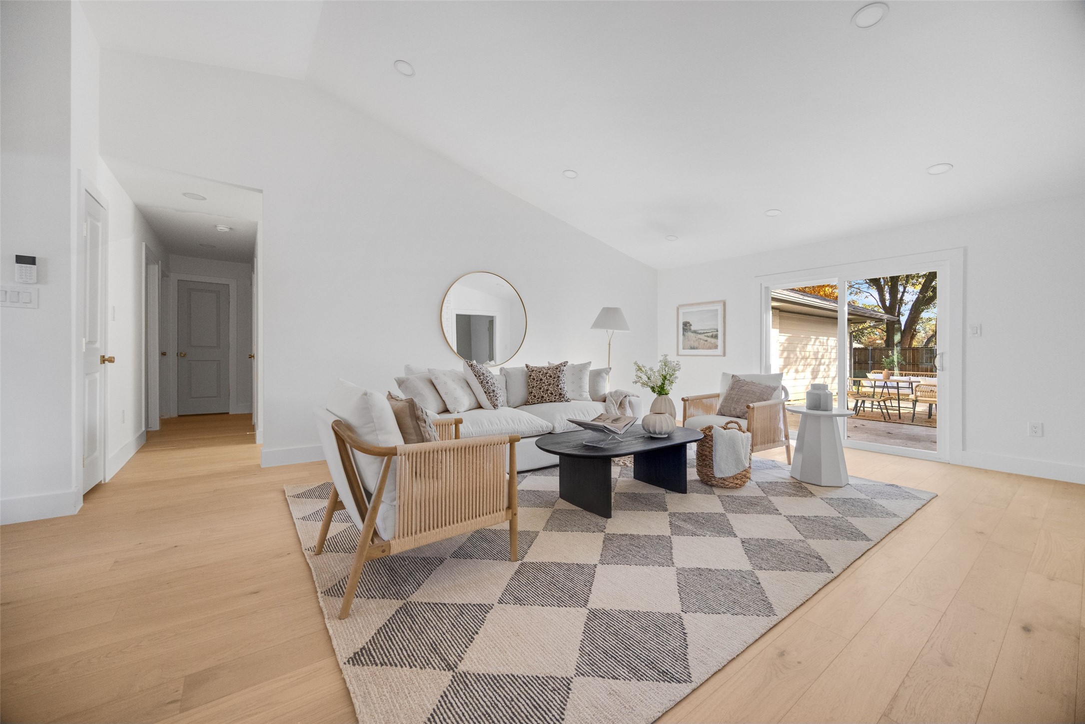 Staged living room with a white sofa, woven chairs, checkered rug, and sliding doors to a patio.