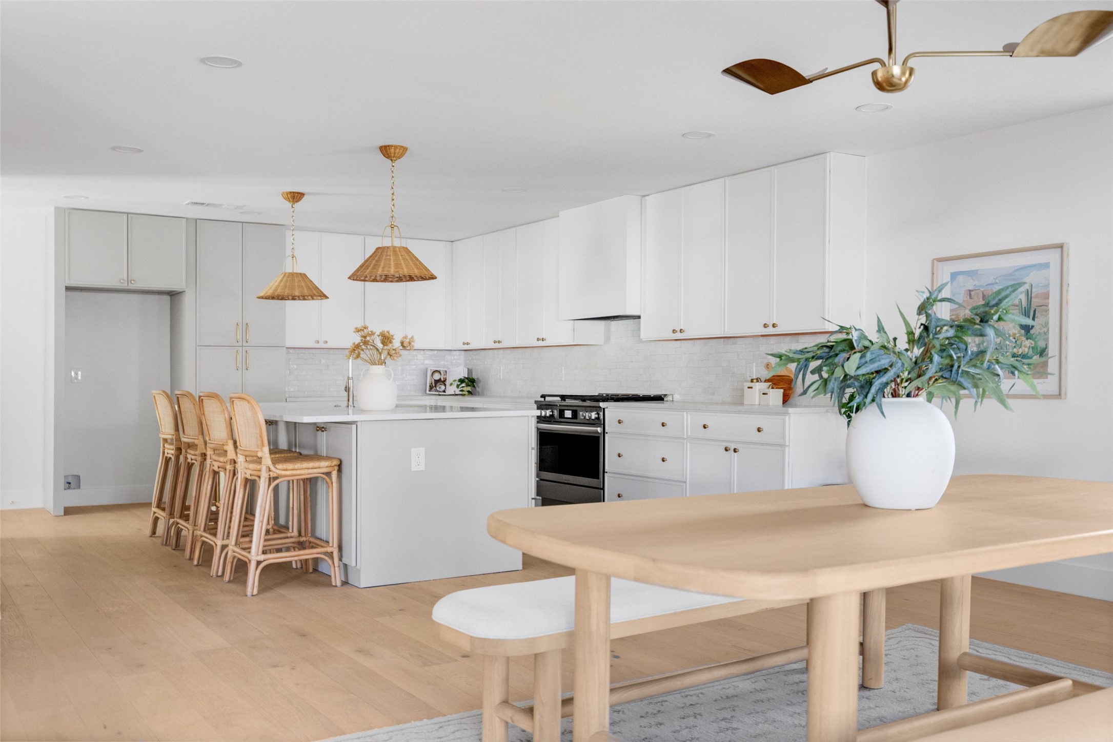 Bright white kitchen with a large island, rattan stools, and an adjoining dining table.