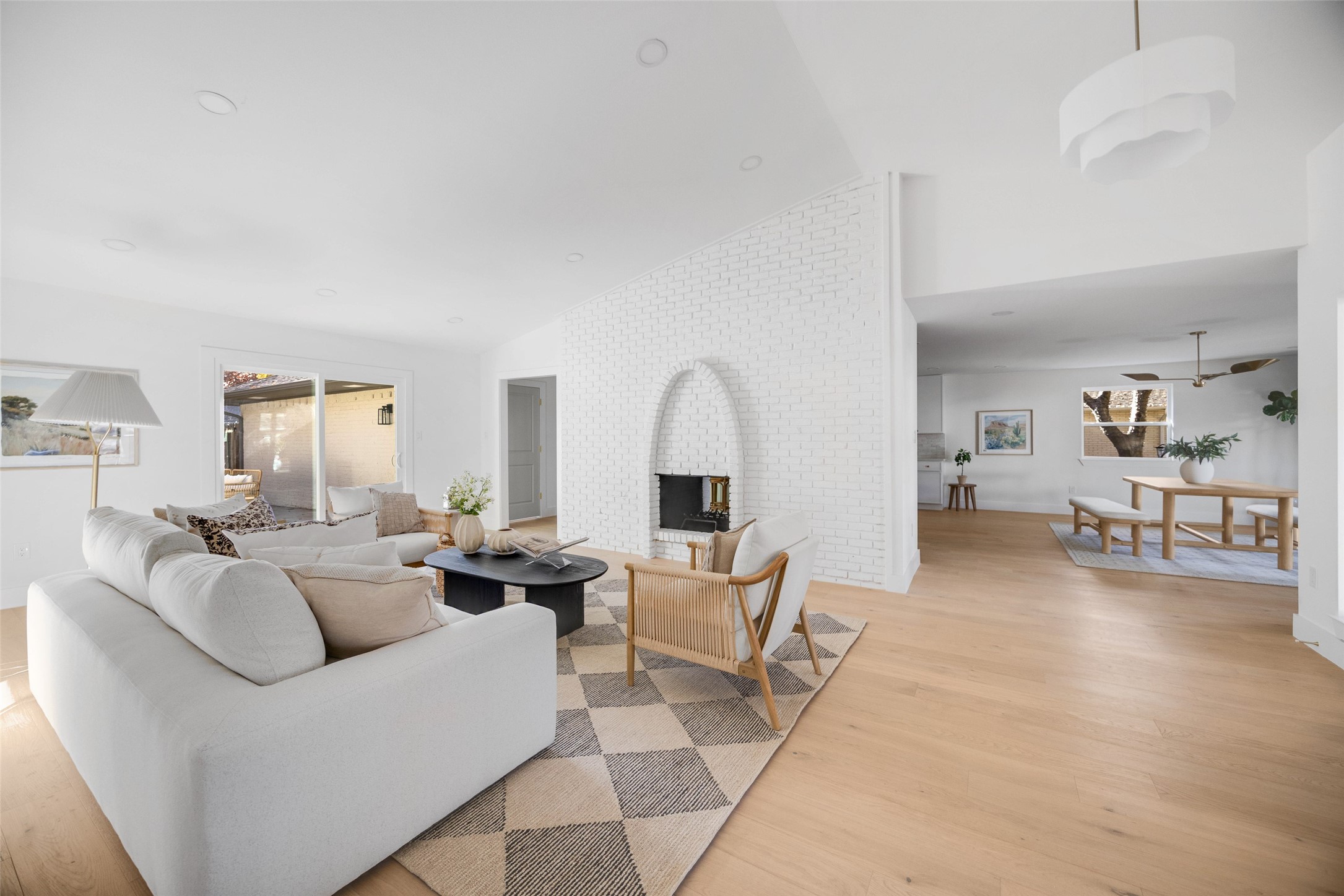 Open-plan living room with a white brick fireplace, neutral sectional, and adjoining dining area.