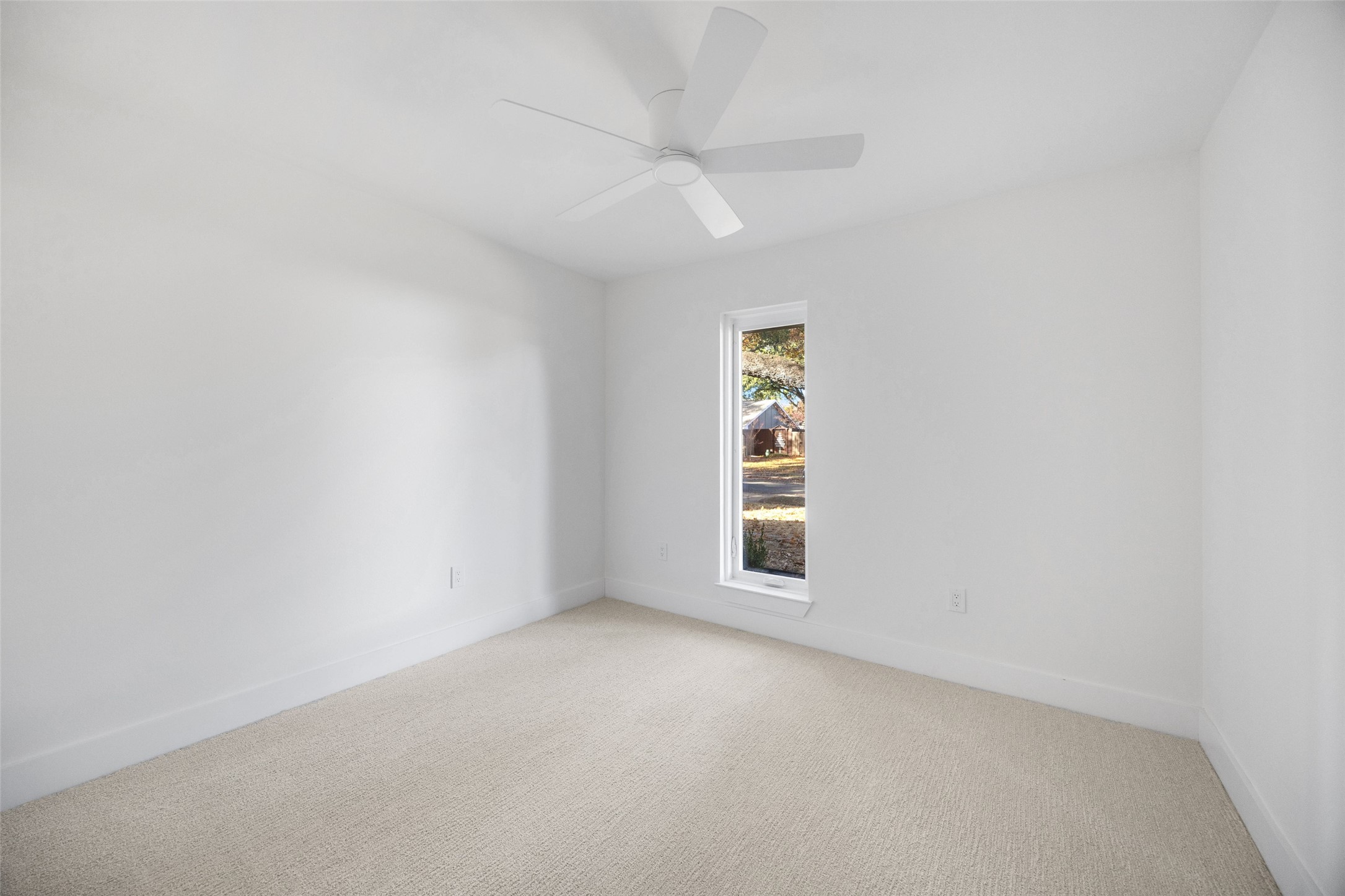 Empty bedroom with beige carpet, a white ceiling fan, and a tall narrow window.