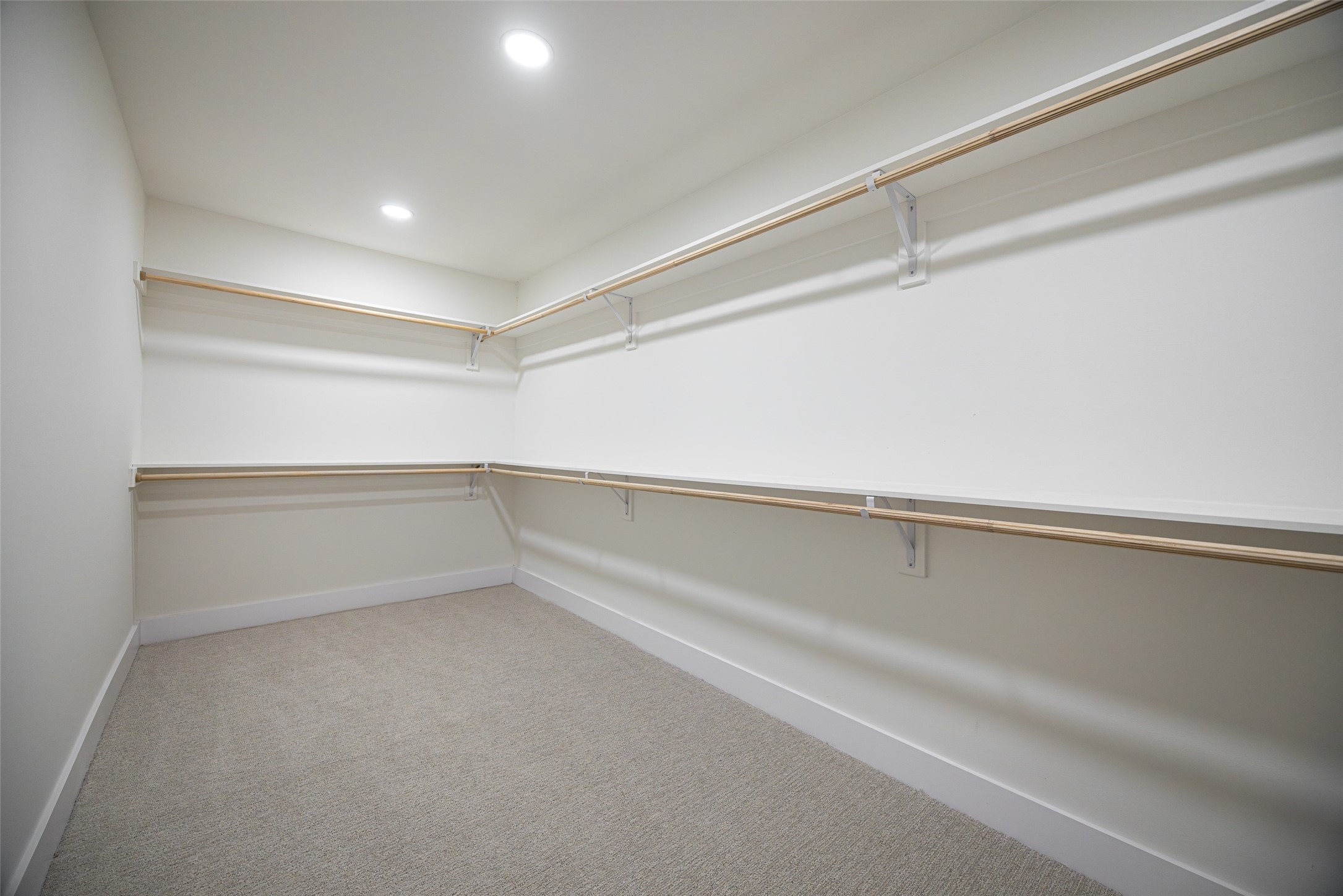 Empty walk-in closet with beige carpet and wraparound wooden hanging rods.