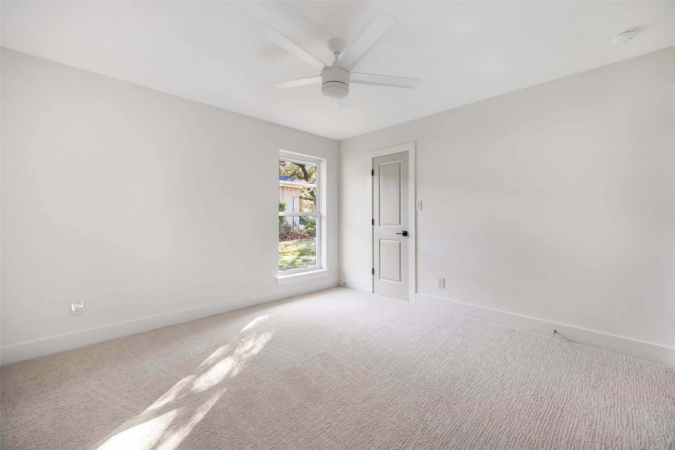 Empty bedroom with light carpet, a ceiling fan, and sunlight streaming through the window.