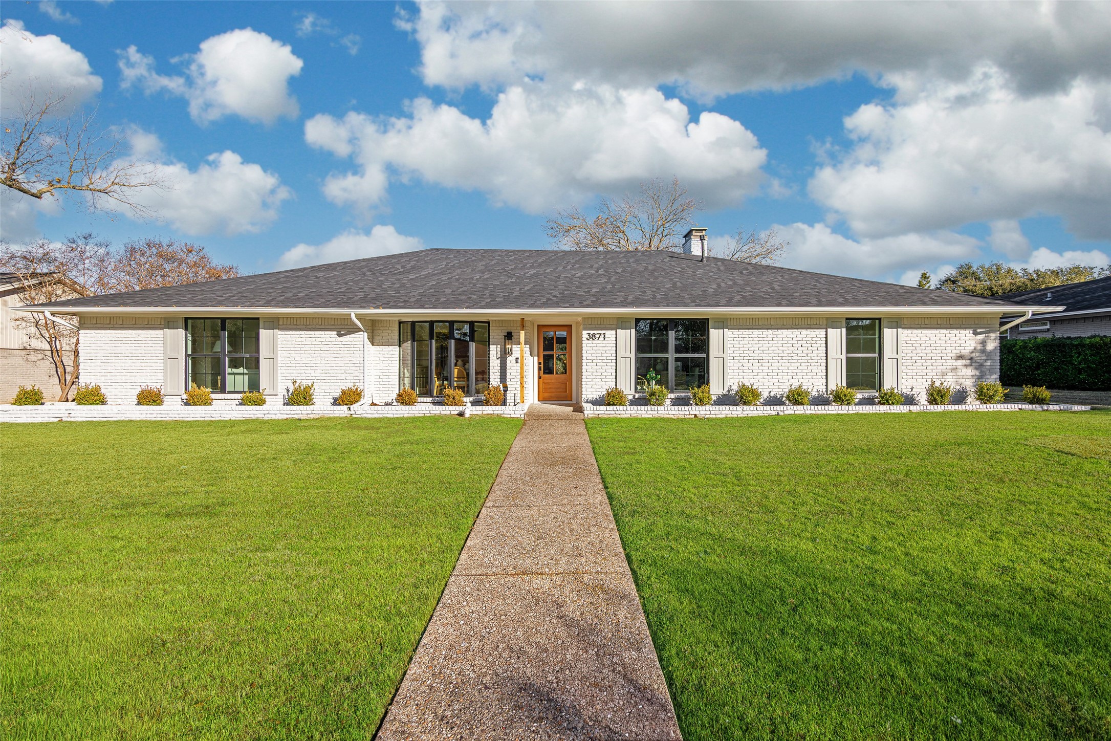 Single-story white brick house with a broad lawn and walkway leading to its wood front door.