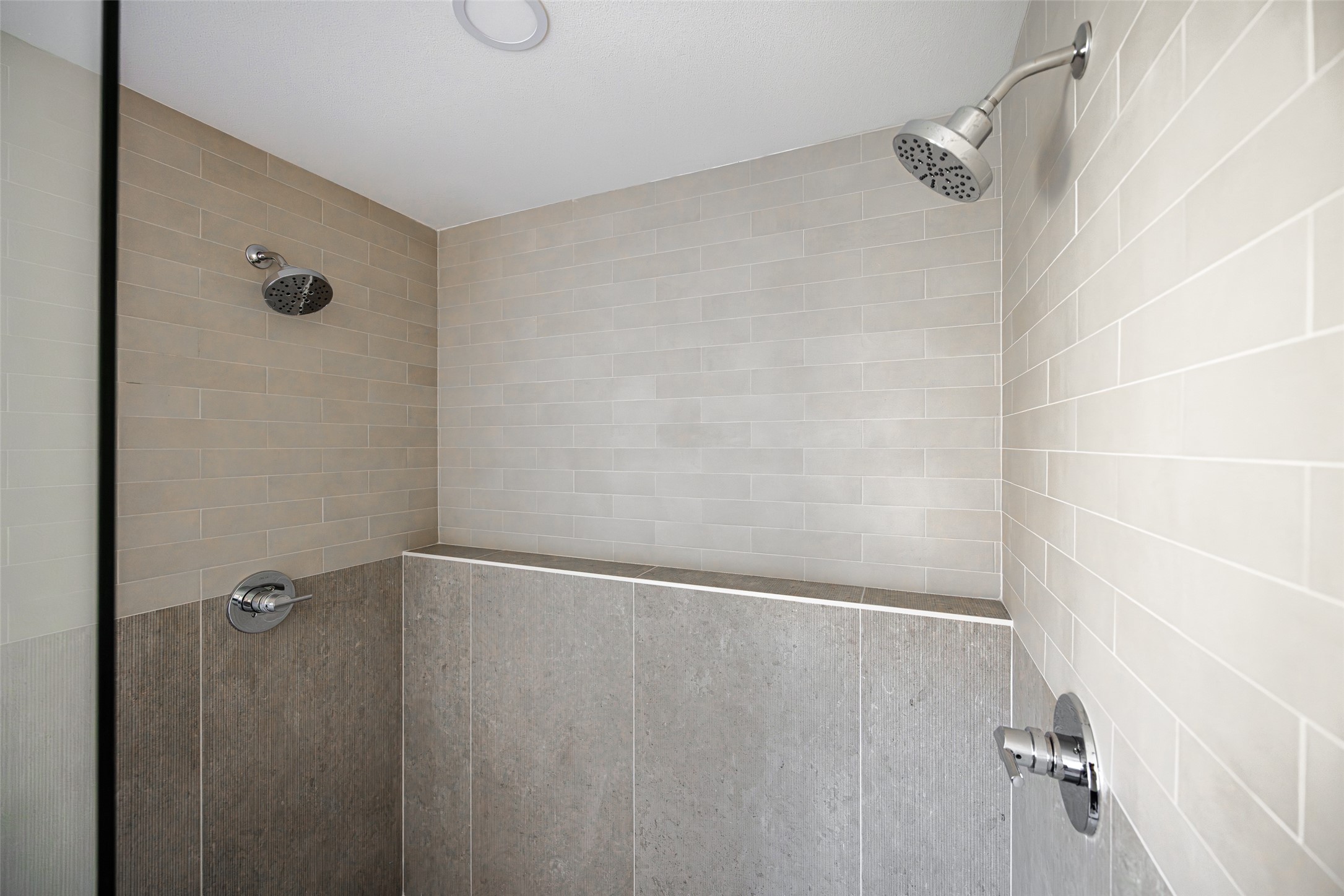 Tiled walk-in shower with two showerheads and chrome fixtures.