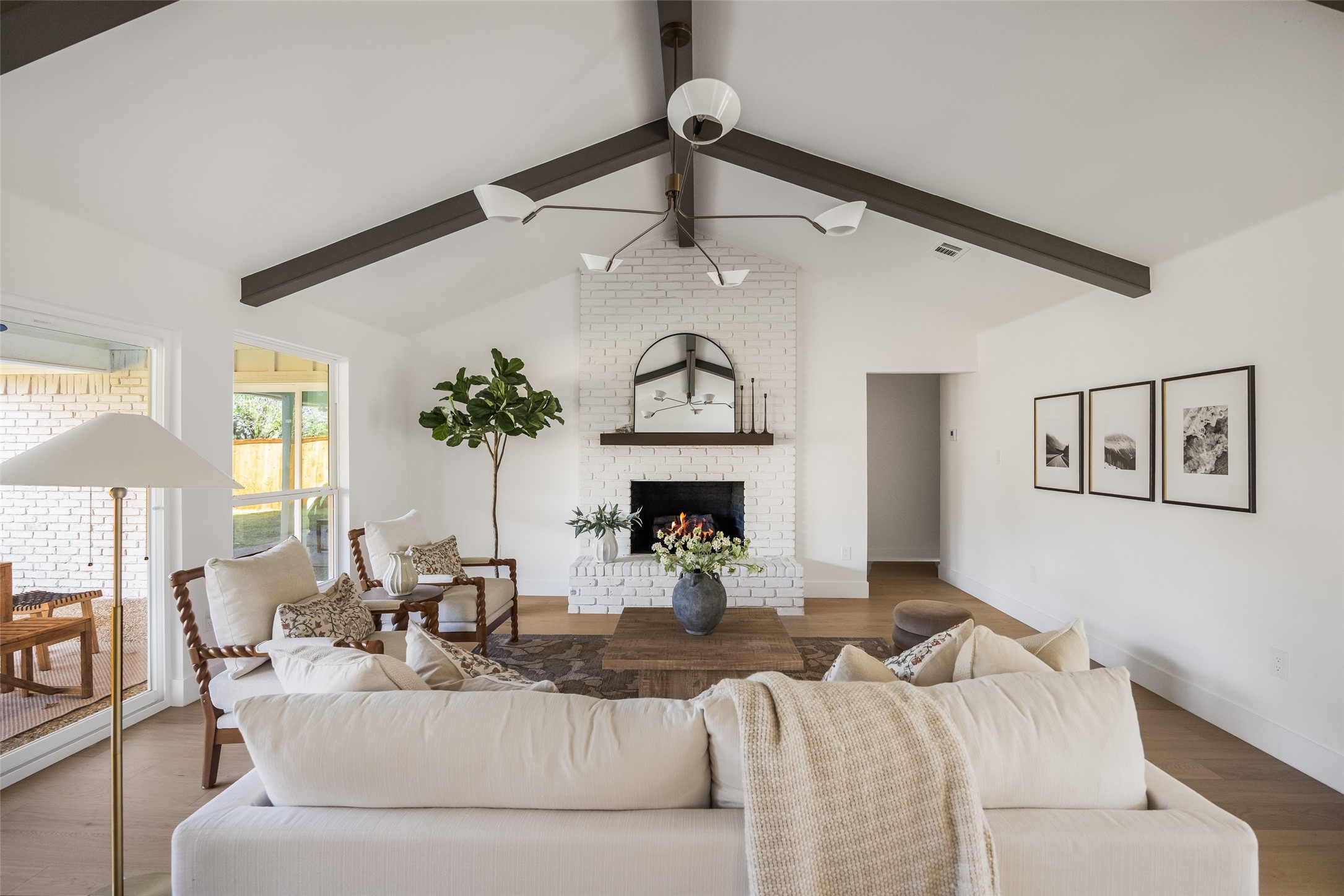 Staged living room with vaulted beamed ceiling, white brick fireplace, and cream seating.