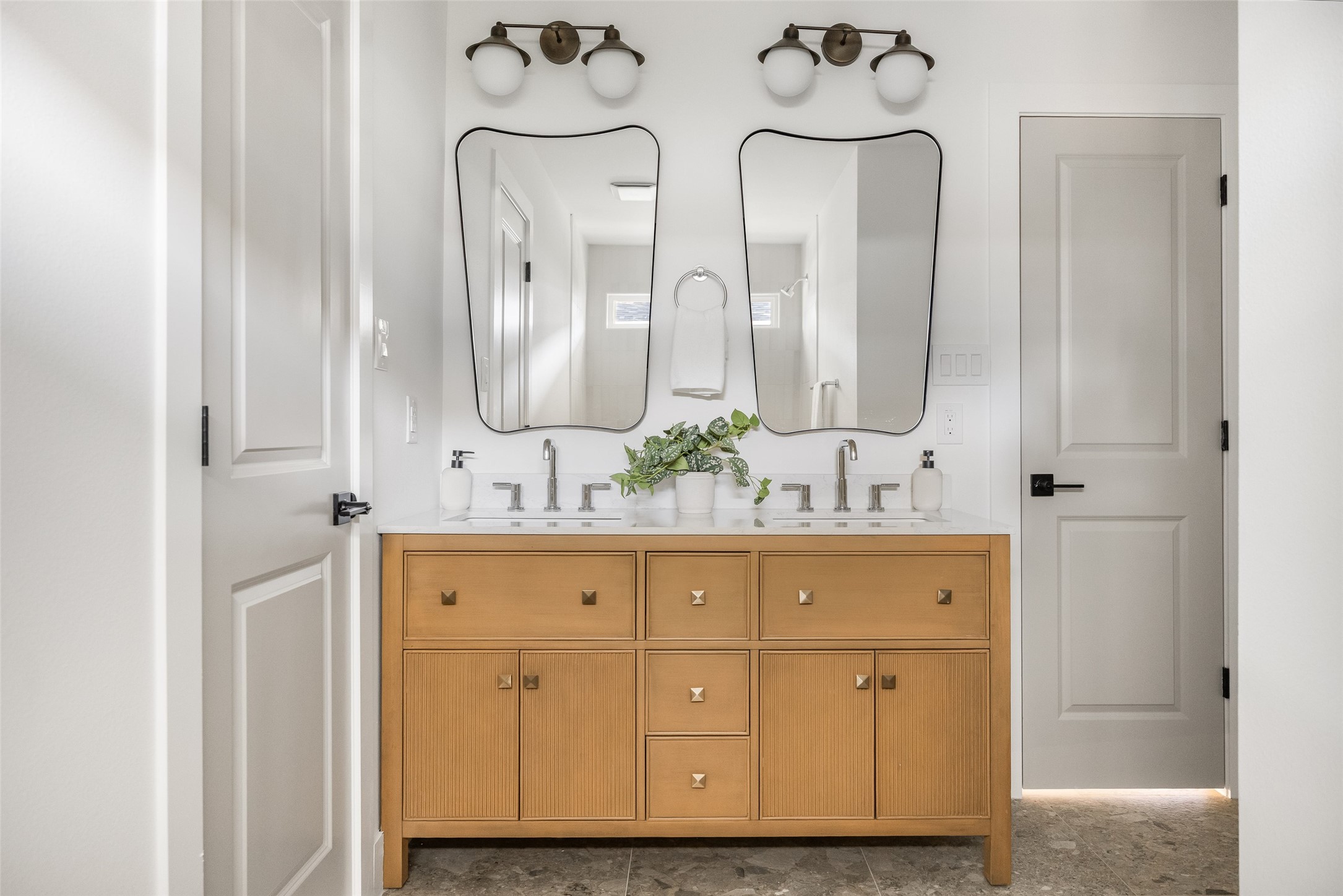 Bathroom with a double-sink wood vanity, paired mirrors, and warm metal lighting.