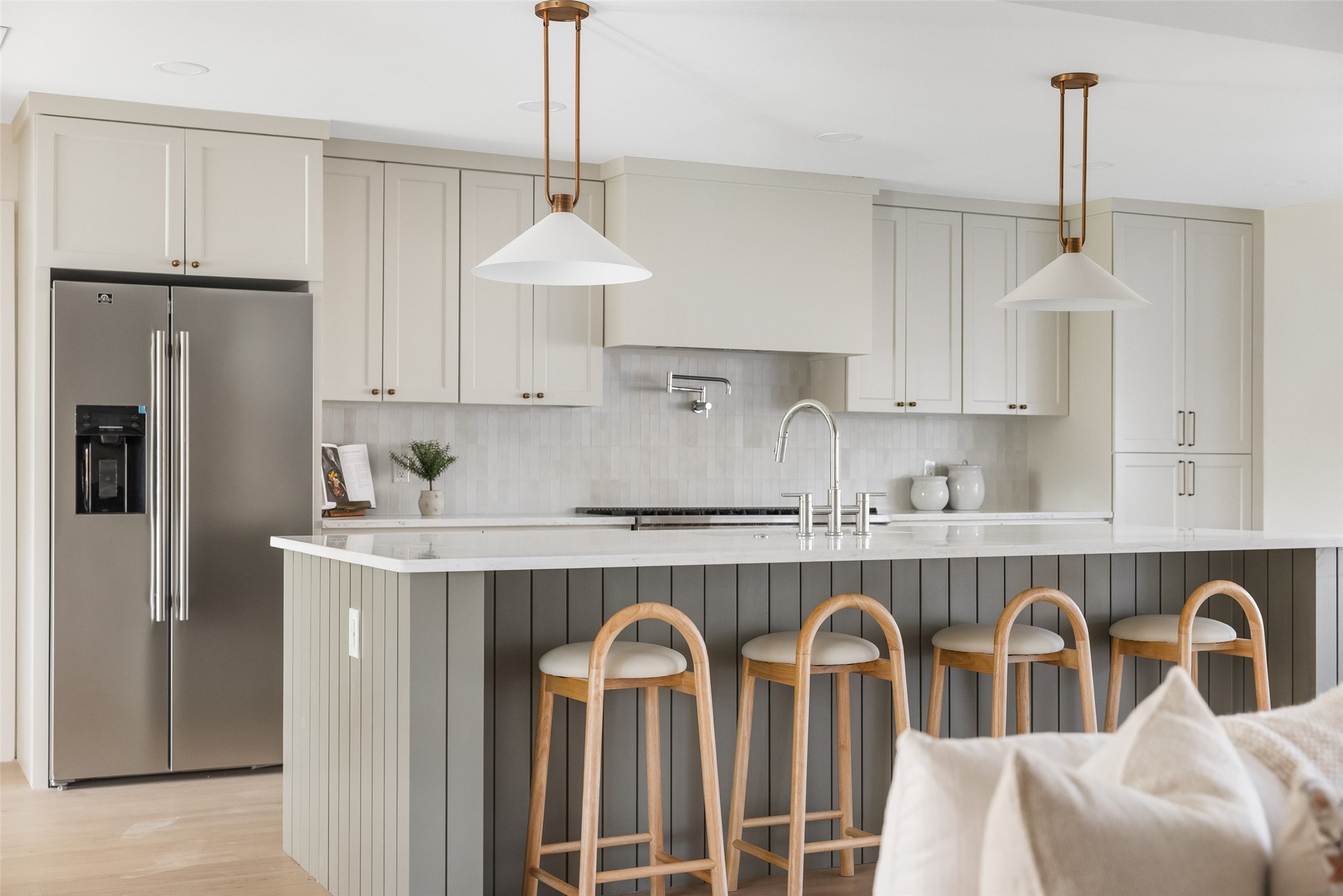 Modern kitchen with a large dark-paneled island, white counters, and four wooden bar stools.