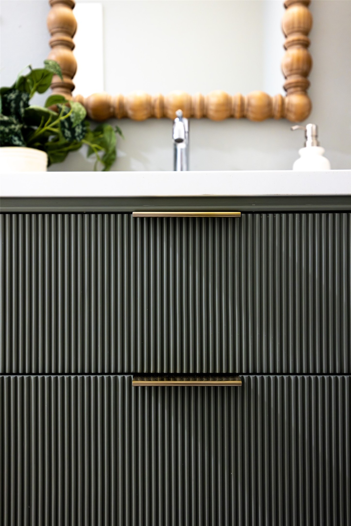 Bathroom vanity with dark fluted cabinets, brass pulls, white countertop, and wooden-framed mirror