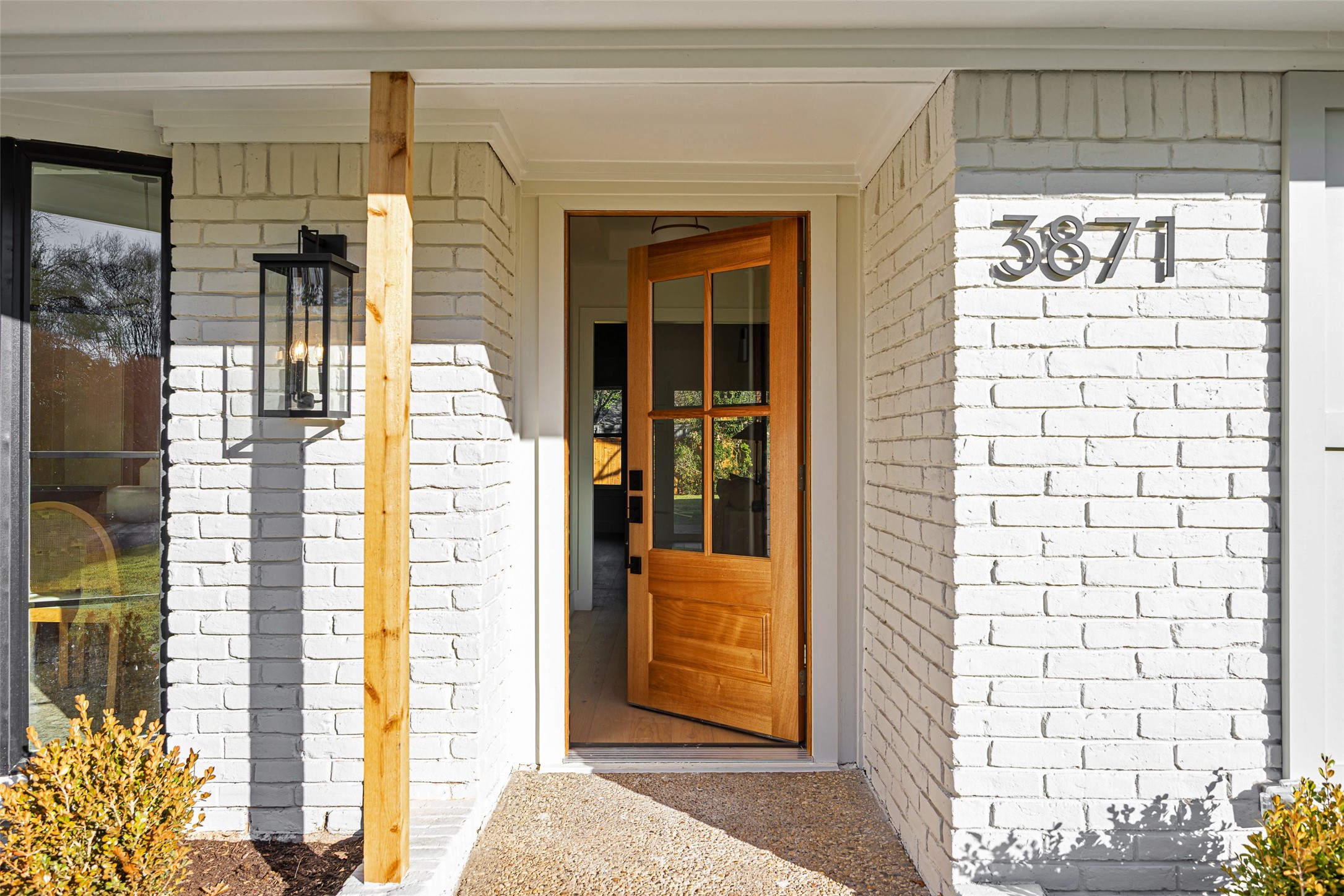 White brick home entrance with an open wood-and-glass door and house number 3871.