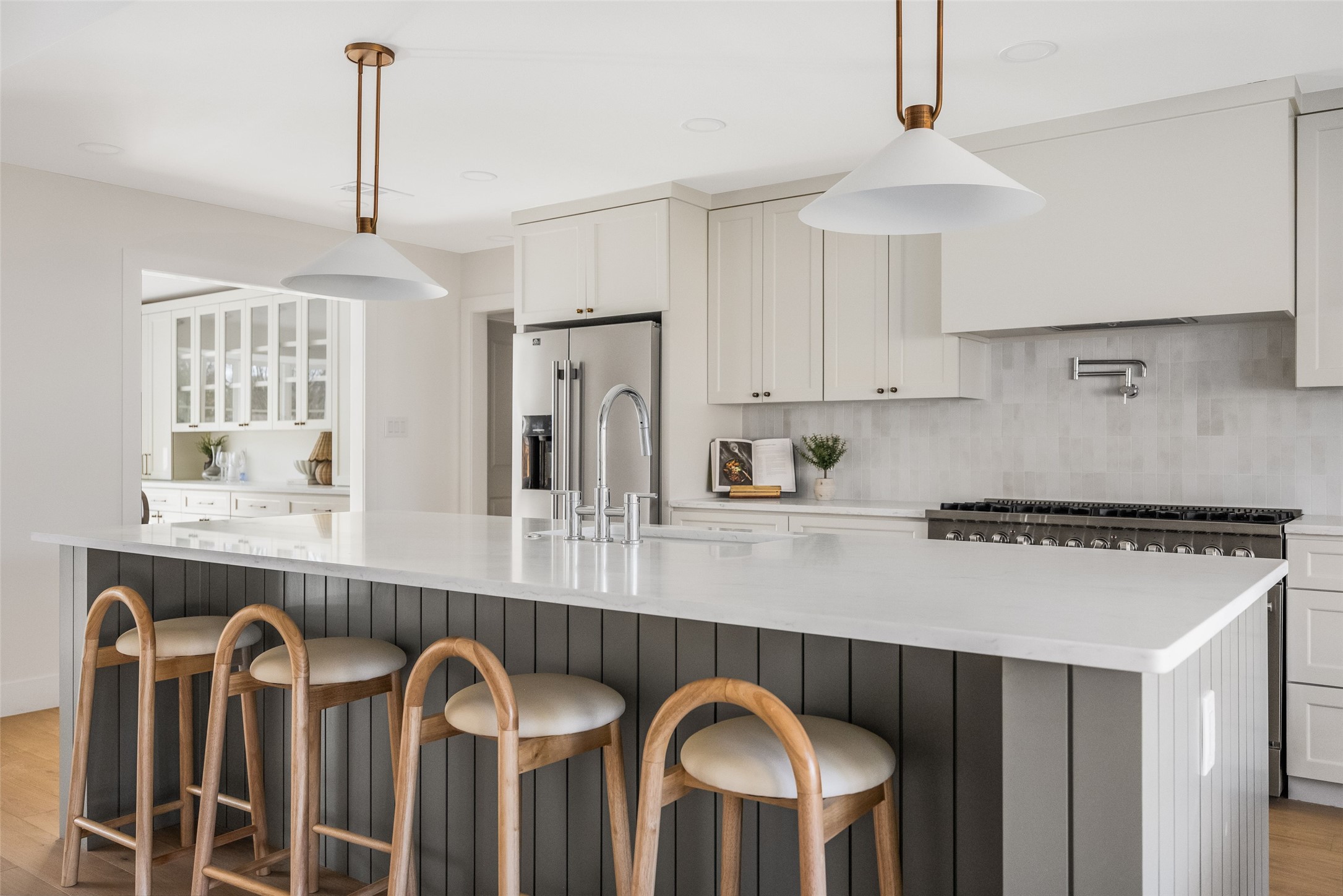 Renovated kitchen with a large quartz island, four wooden stools, and white cabinetry.