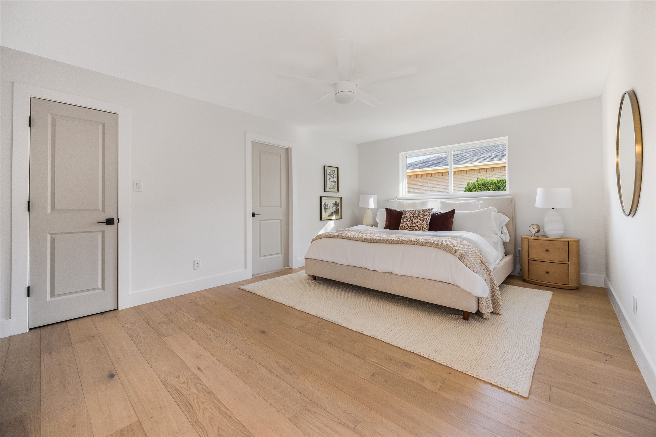 Staged bedroom with a king bed beneath a window, light oak floors, and a cream rug.