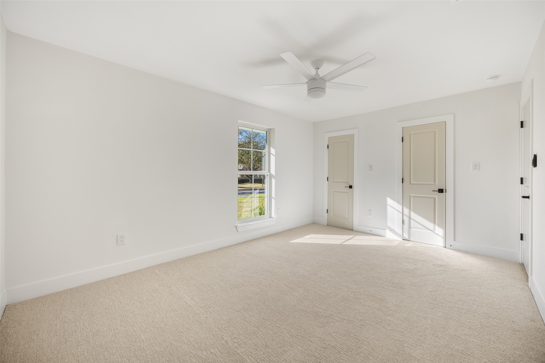 Vacant carpeted room with a ceiling fan, one window, and two paneled doors.