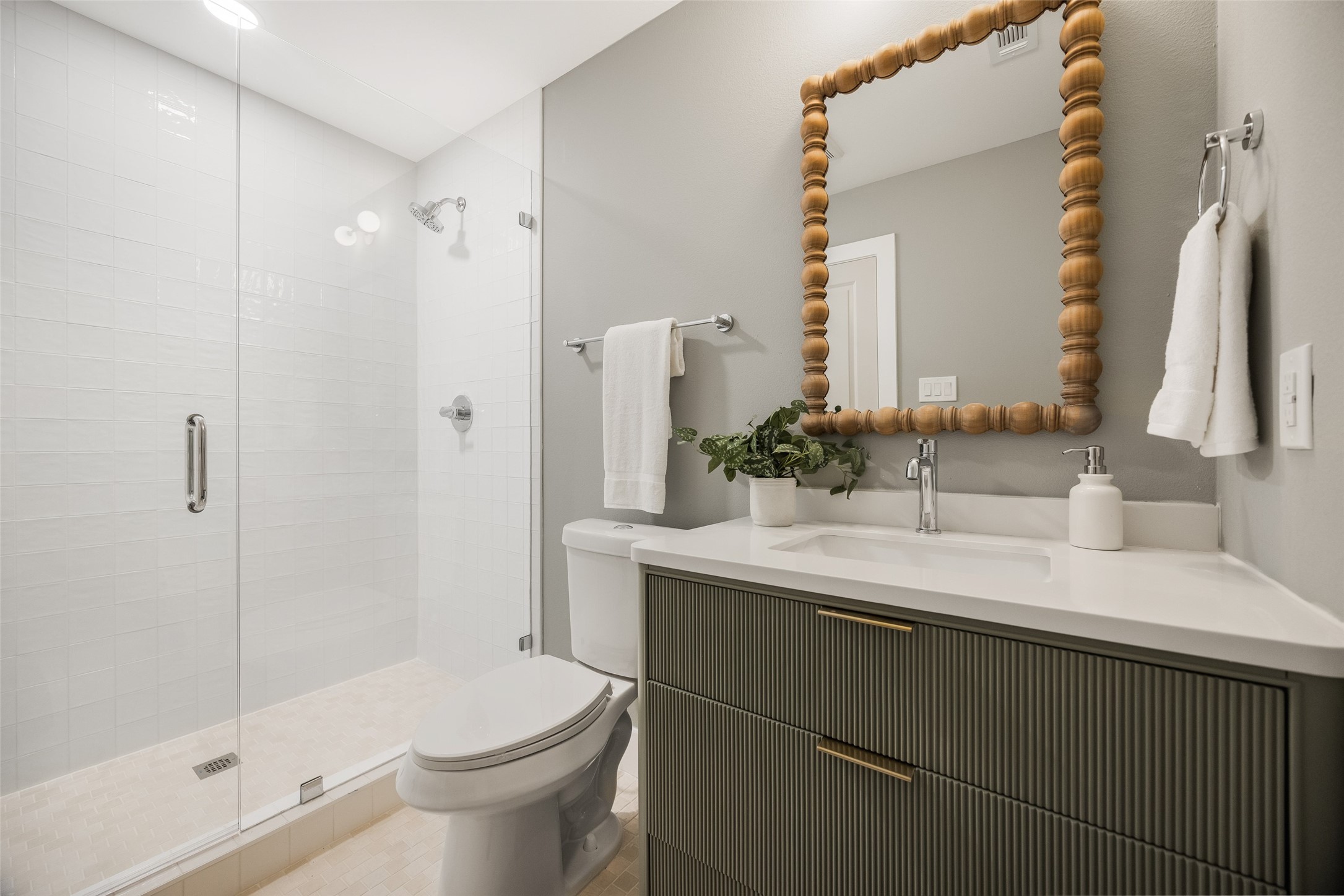 Bathroom with a glass-enclosed white tiled shower and dark ribbed vanity beneath a large wood-framed mirror.
