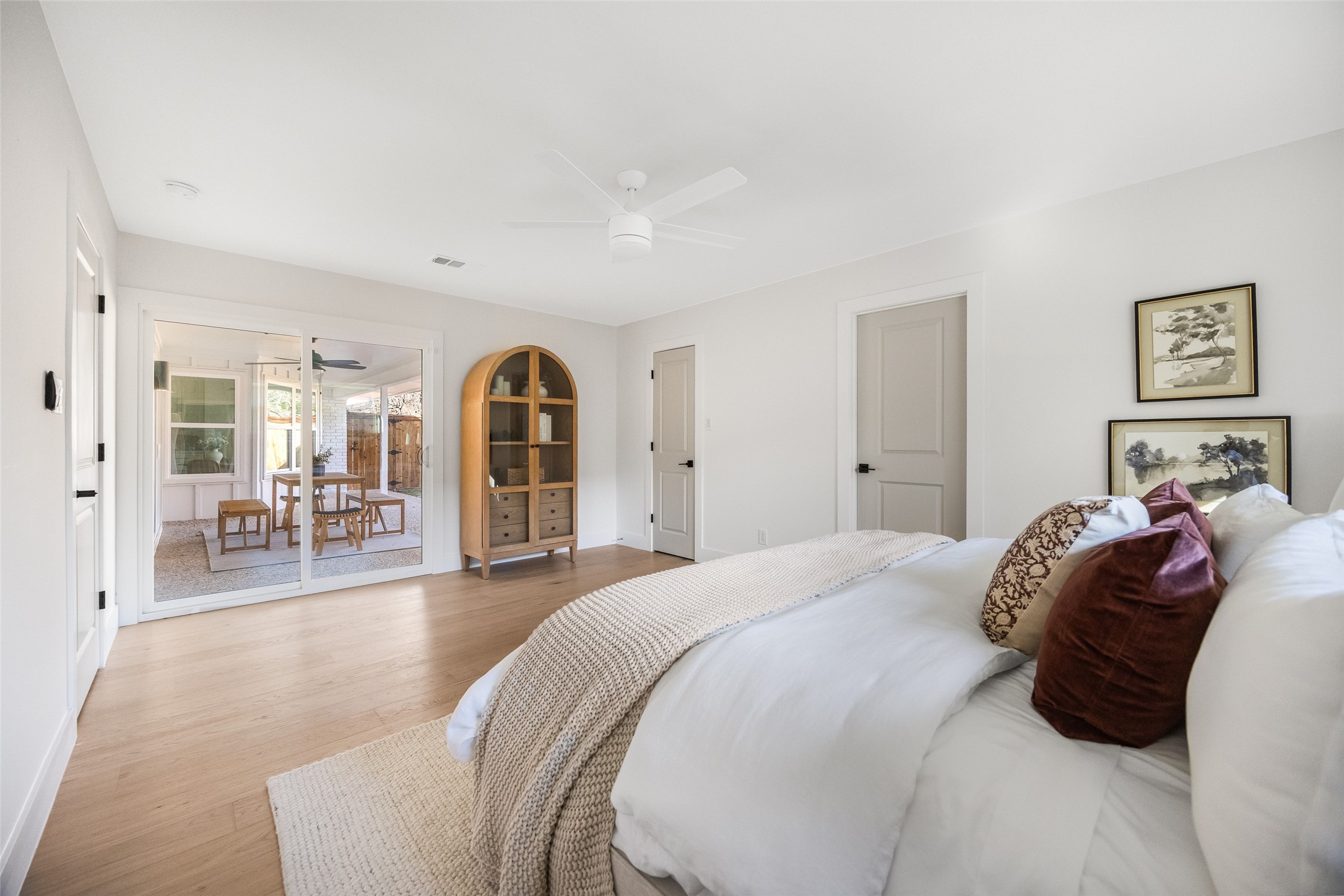 Bedroom with a white bed, burgundy pillows, and sliding doors opening to a covered patio.