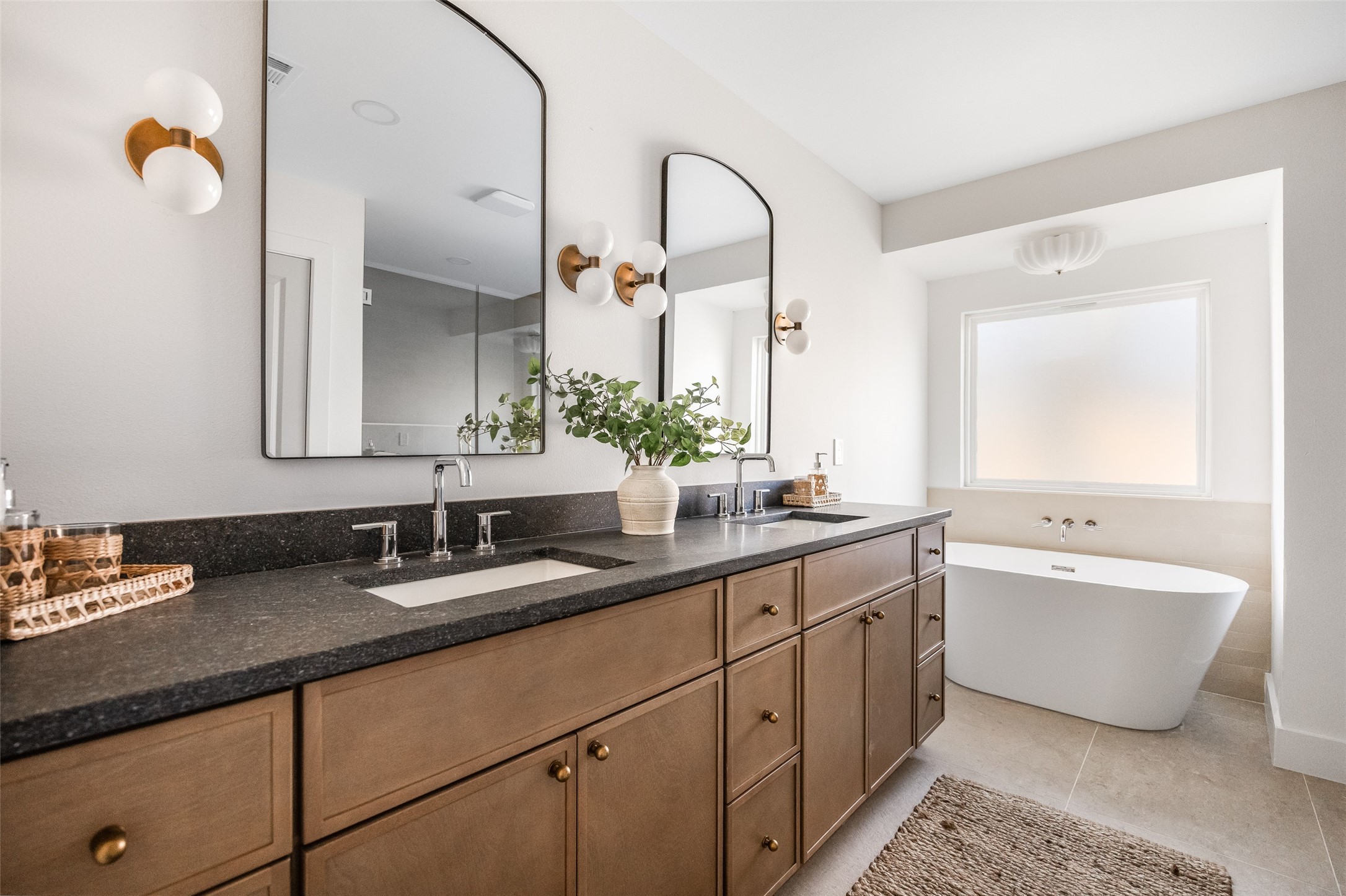 Bathroom with a double-sink wood vanity and freestanding tub beneath a large window.