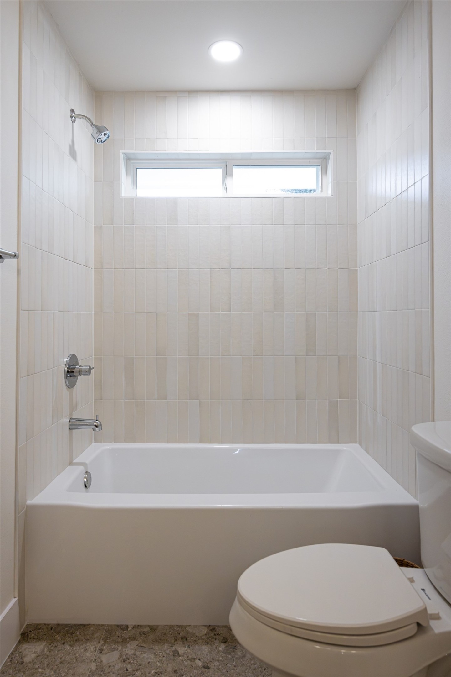 Bathroom with a white bathtub, tiled surround, narrow window, and toilet.
