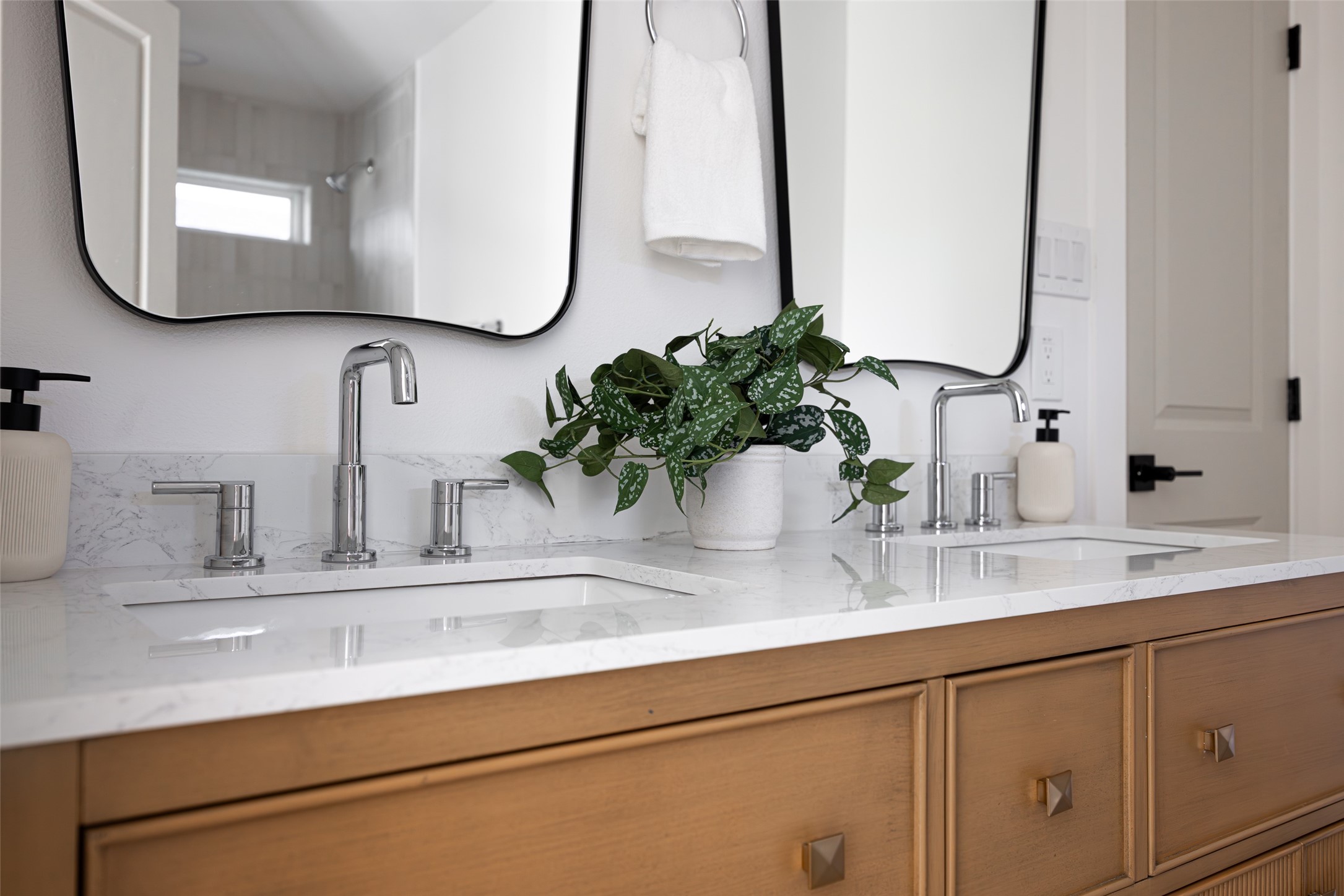 Bathroom vanity with double sinks, marble counters, warm wood cabinetry, and large mirrors.