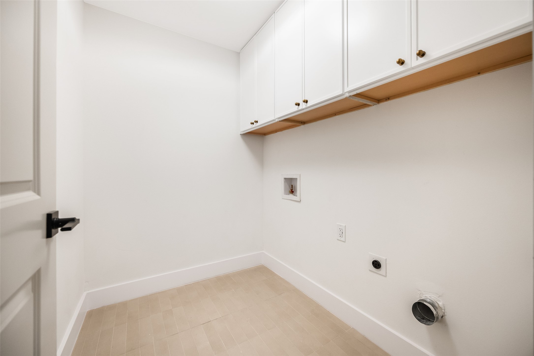 Empty laundry room with overhead cabinets, beige tile flooring, and washer and dryer hookups.