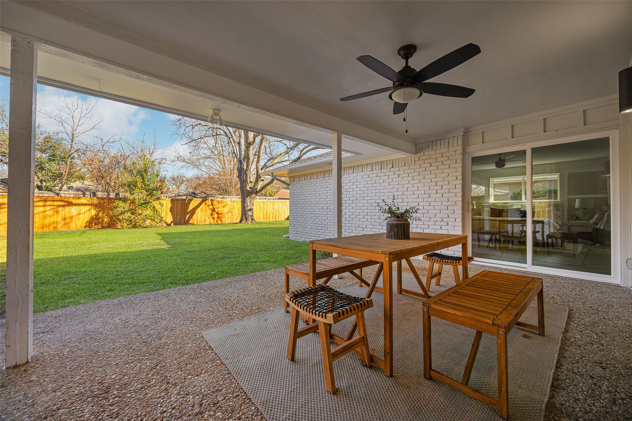 Covered patio with wooden dining set overlooking a fenced green lawn.