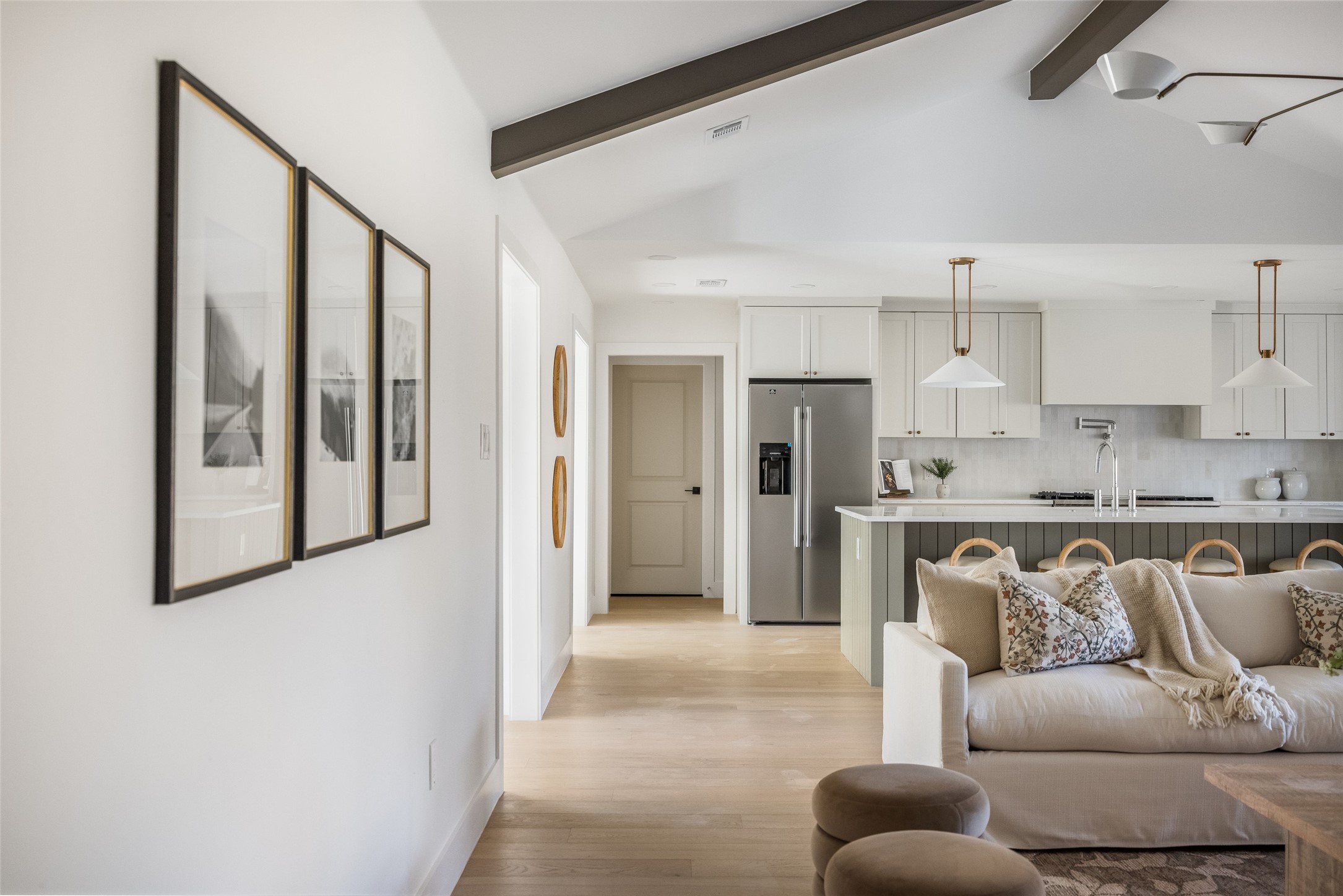 Open-plan kitchen and living room with a large island, white cabinetry, and a neutral sofa.