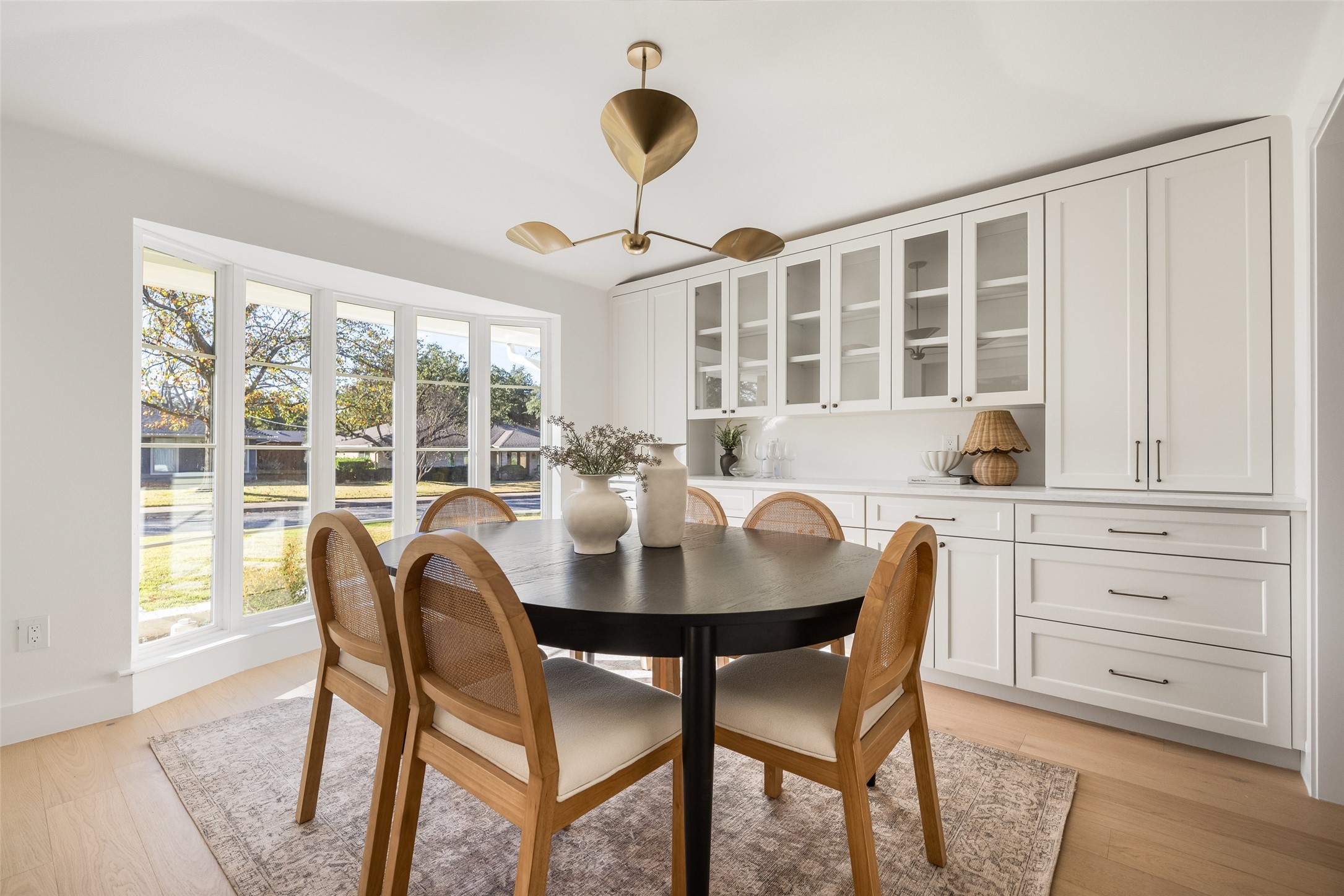 Dining room with a round table, woven chairs, white built-ins, and tall windows.