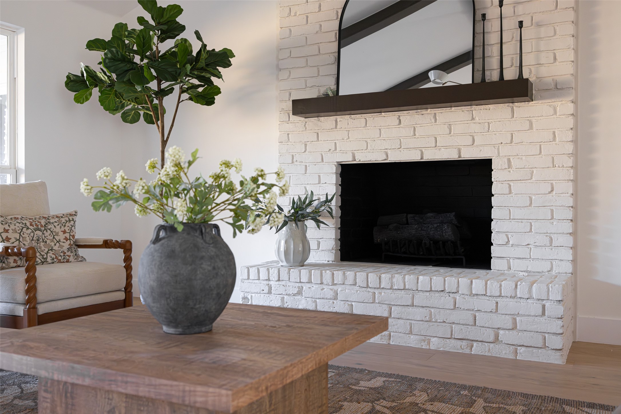 Living room with a white brick fireplace, arched mirror, and wood coffee table with flowers.