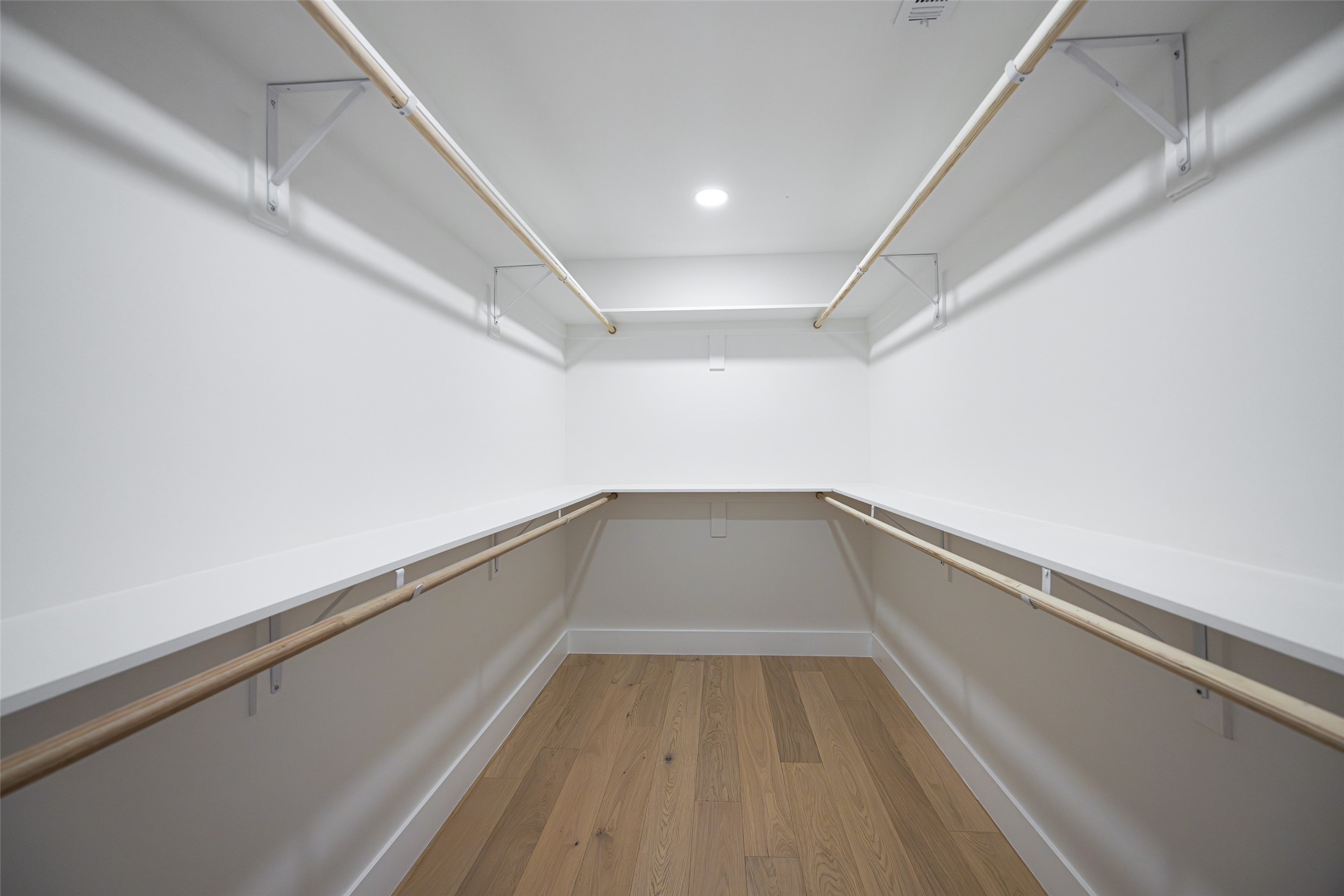 Walk-in closet with wraparound shelves and wooden hanging rods above a light wood floor.