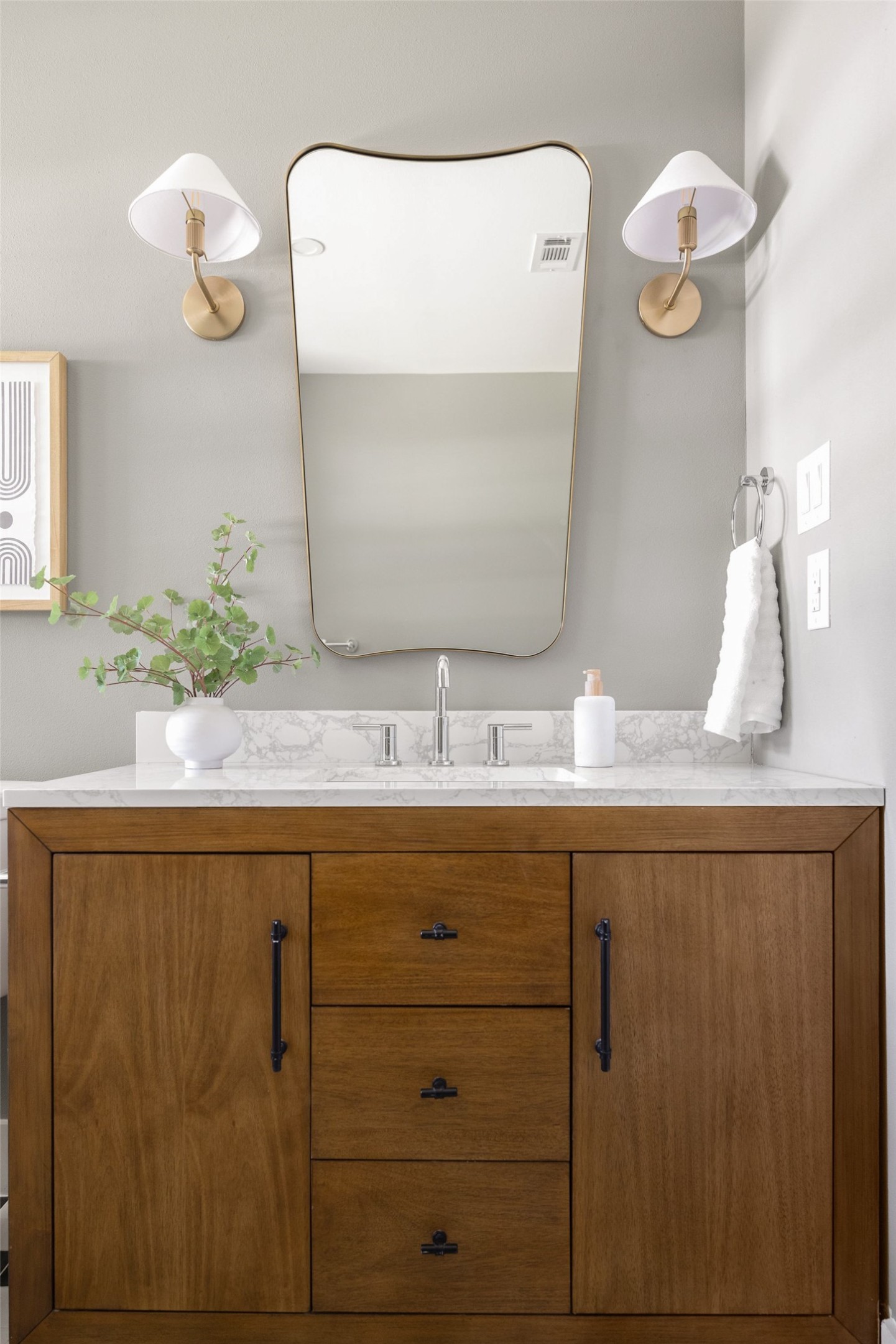Bathroom vanity with a wood cabinet, marble counter, brass sconces, and large mirror.
