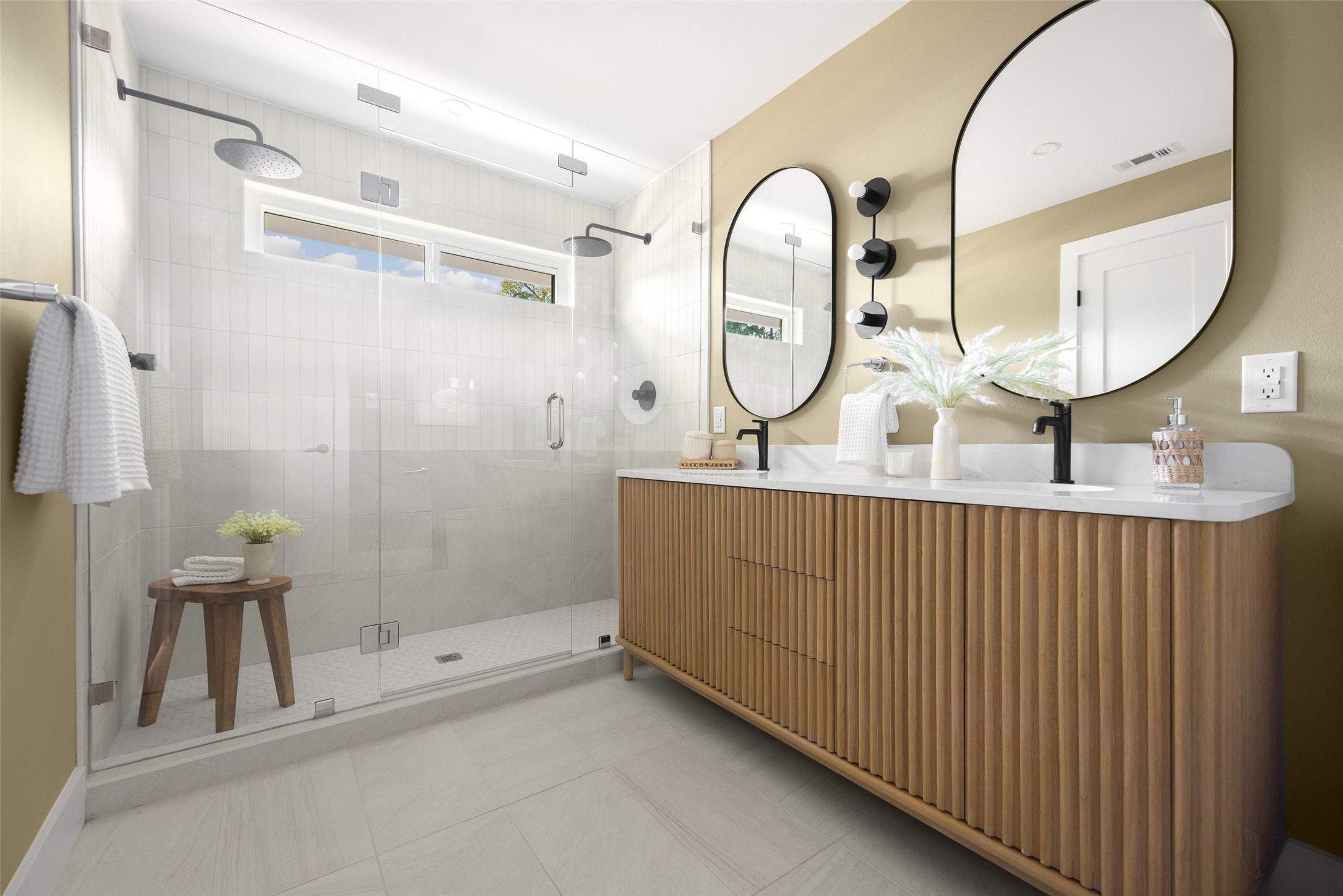 Bathroom with a glass walk-in shower and double wood-slat vanity beneath two oval mirrors.