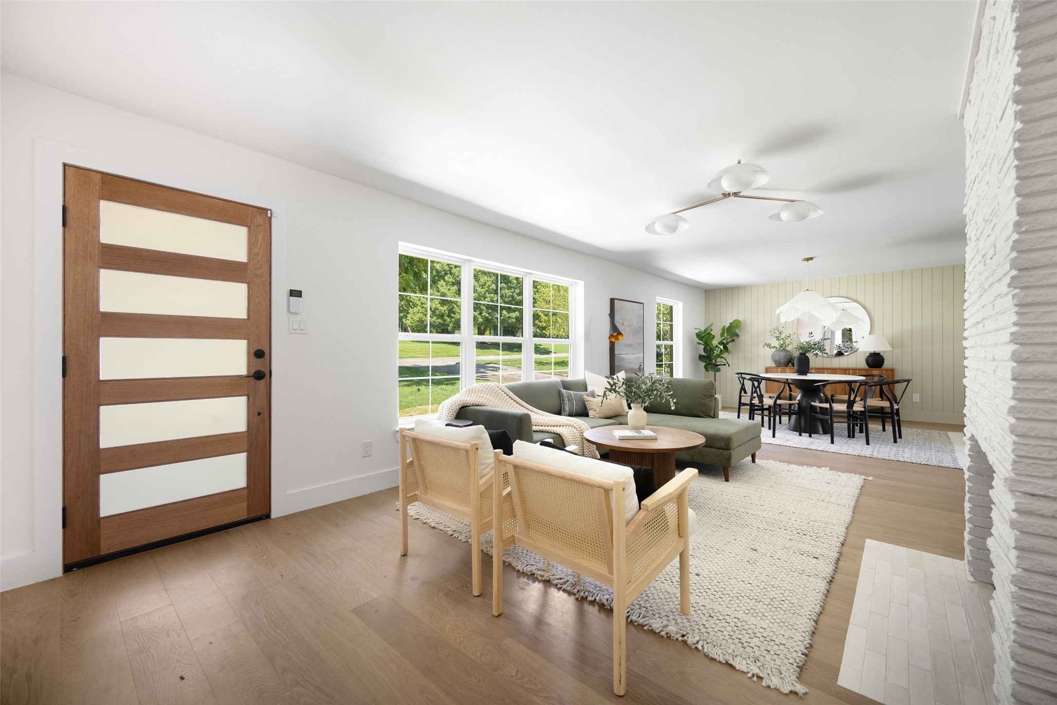 Open-plan living and dining room with a green sectional, large windows, and white brick fireplace.