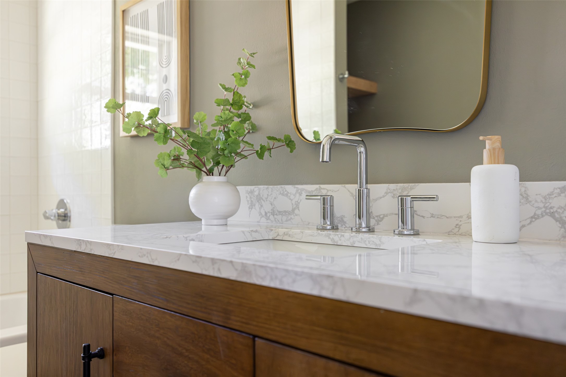 Bathroom vanity with marble-pattern counter, chrome faucet, dark wood cabinets, and a gold-framed mirror.