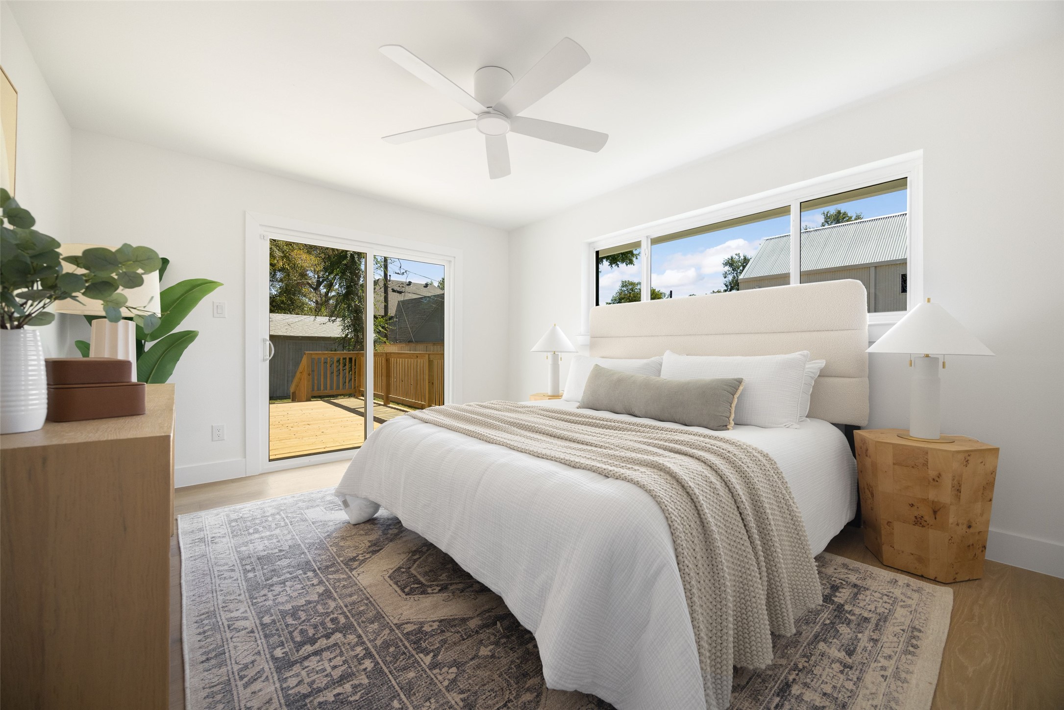 Bright bedroom with a white bed, large windows, and sliding doors opening onto a wooden deck.